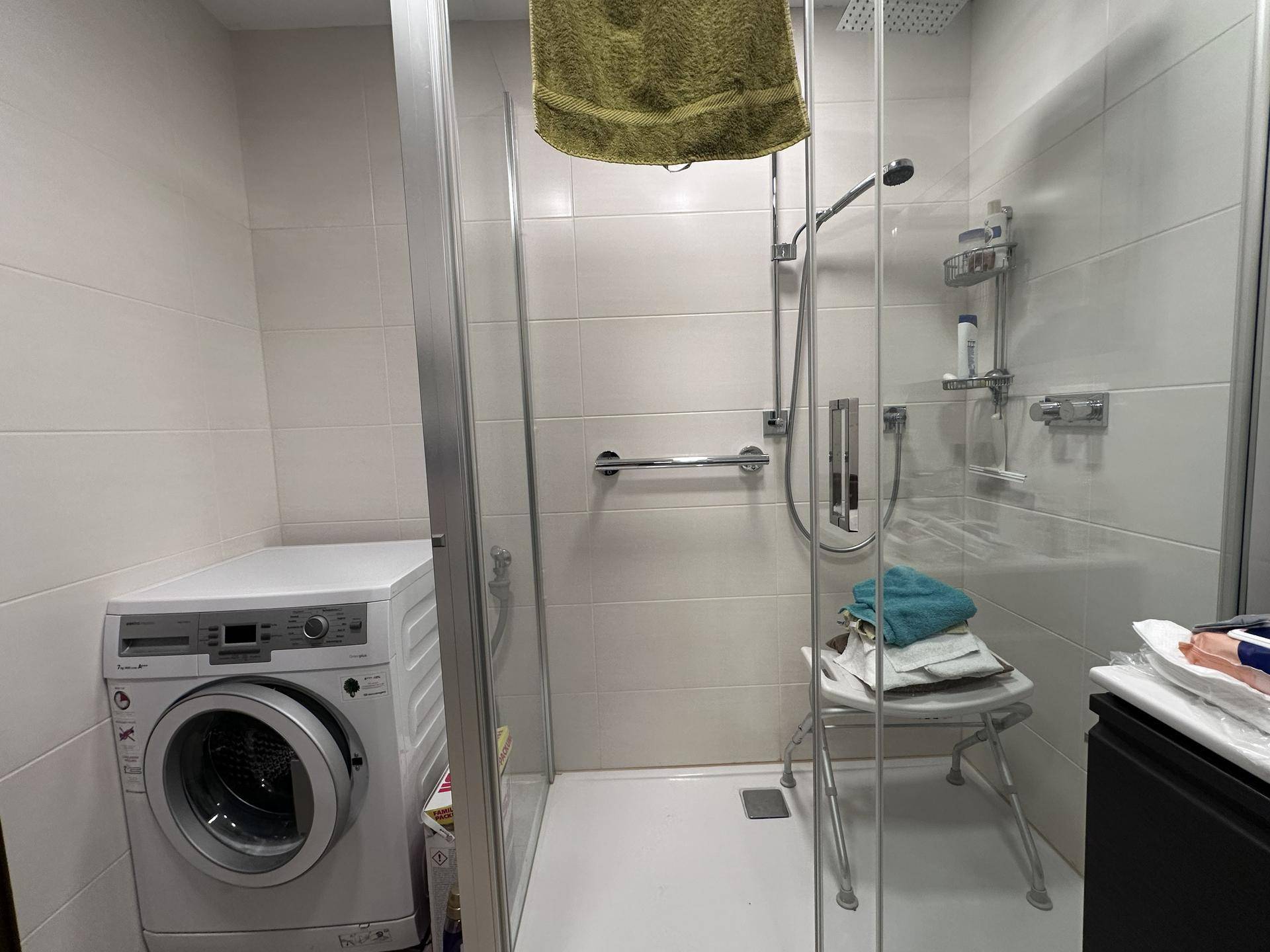 Duschbereich mit Glasabtrennung, Haltegriffen und Waschmaschine im Badezimmer.