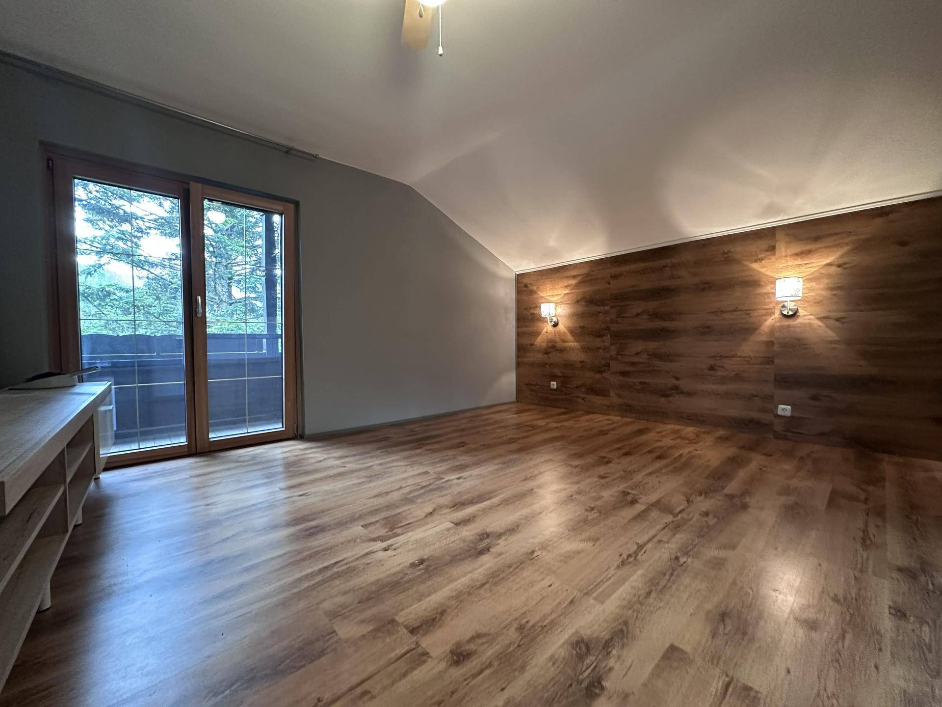 Geräumiges Schlafzimmer mit Holzlaminatboden, Holzwandverkleidung und Zugang zum Balkon.