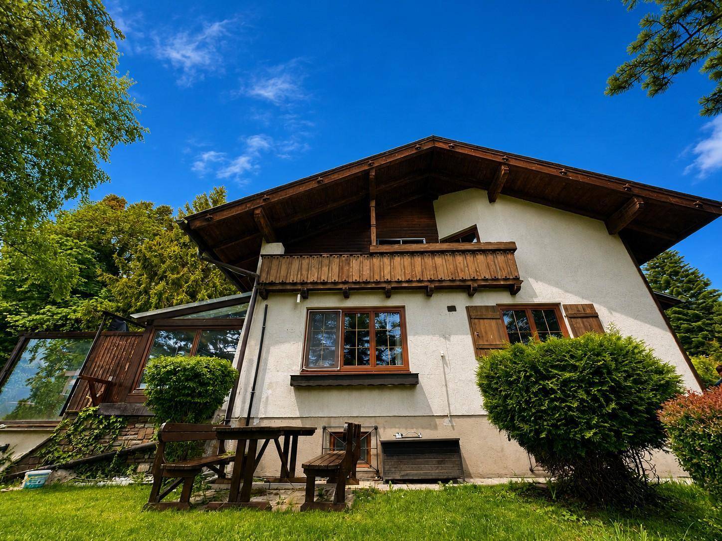 Traditionelles Haus mit Holzbalkonen, Wintergarten und rustikalen Gartenmöbeln im Grünen.