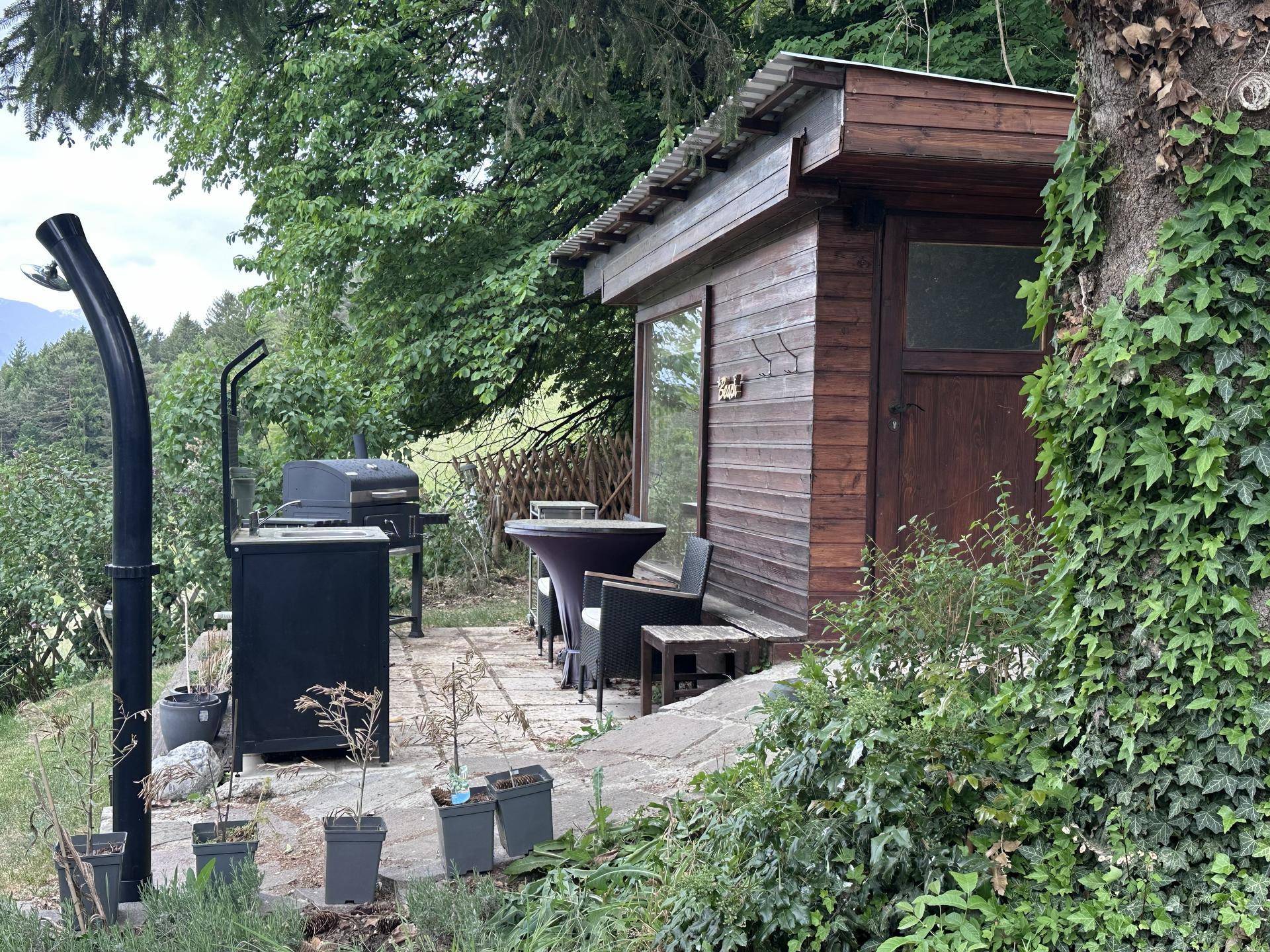 Gemütliche Gartenhütte mit Grillplatz und kleiner Terrasse, umgeben von viel Grün.