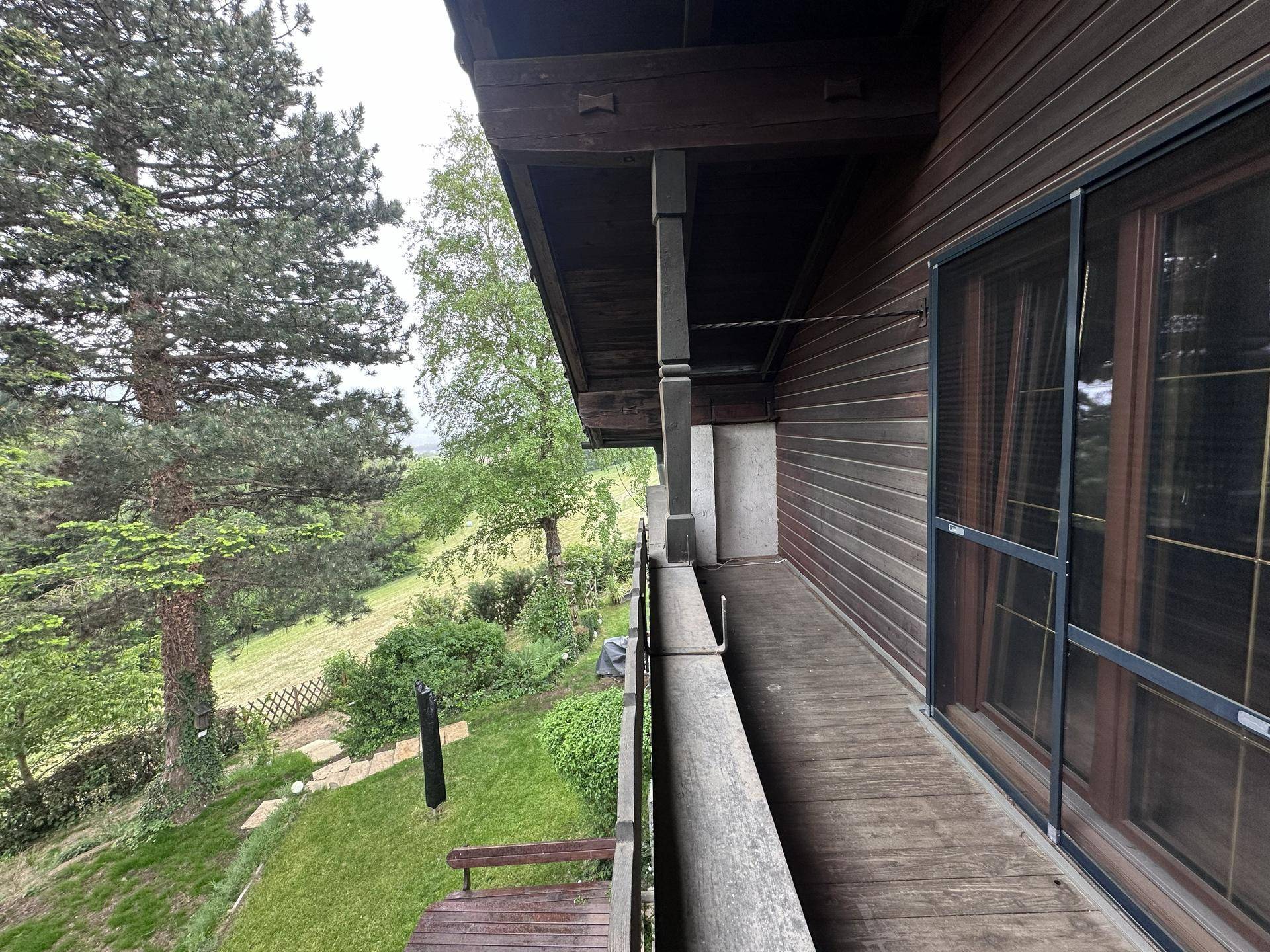 Langer Holzbalkon mit Blick auf die grüne Landschaft und die umliegenden Bäume.