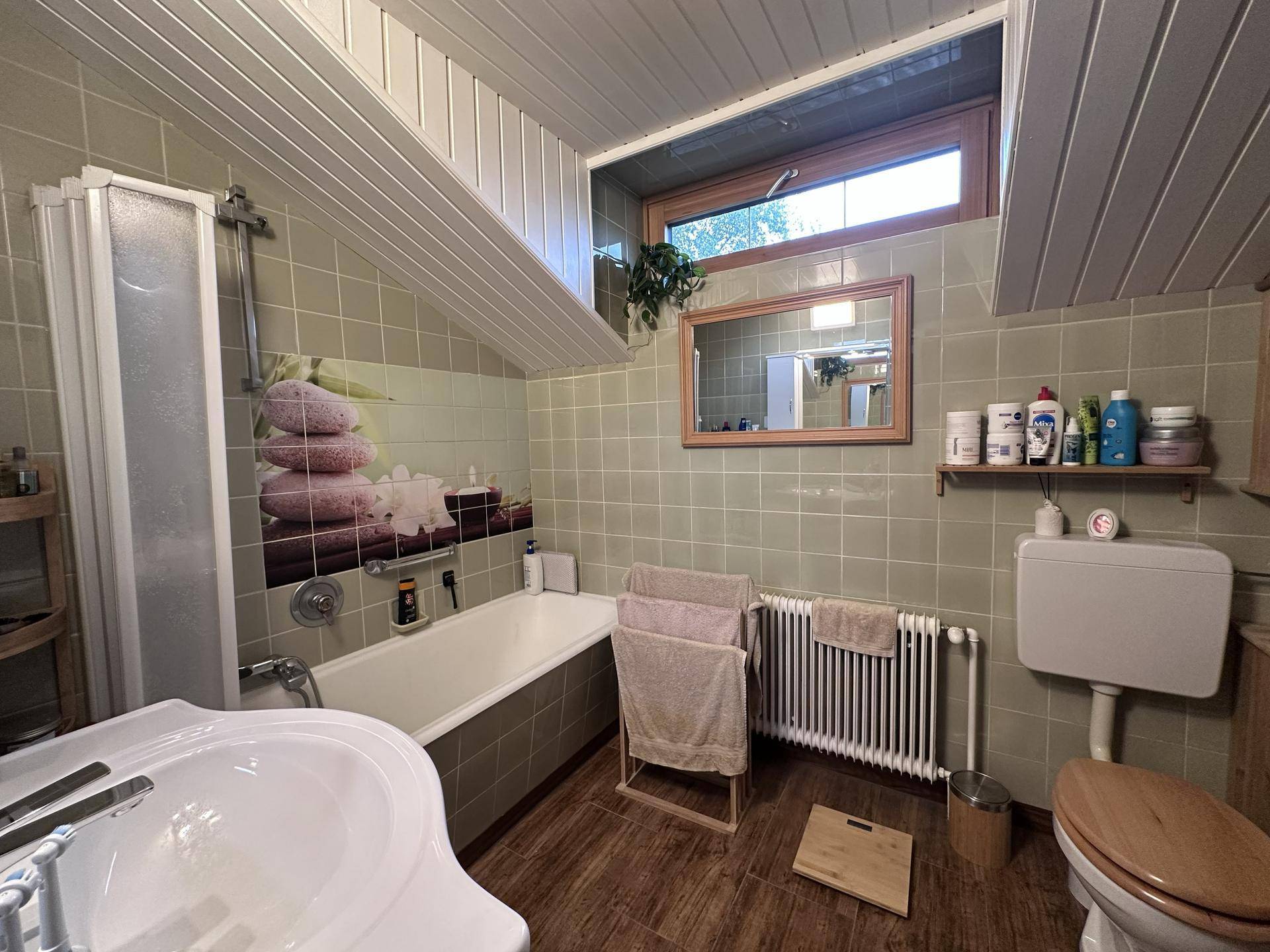 Badezimmer mit Dusche, Badewanne, WC und Fenster, in einem älteren Stil.