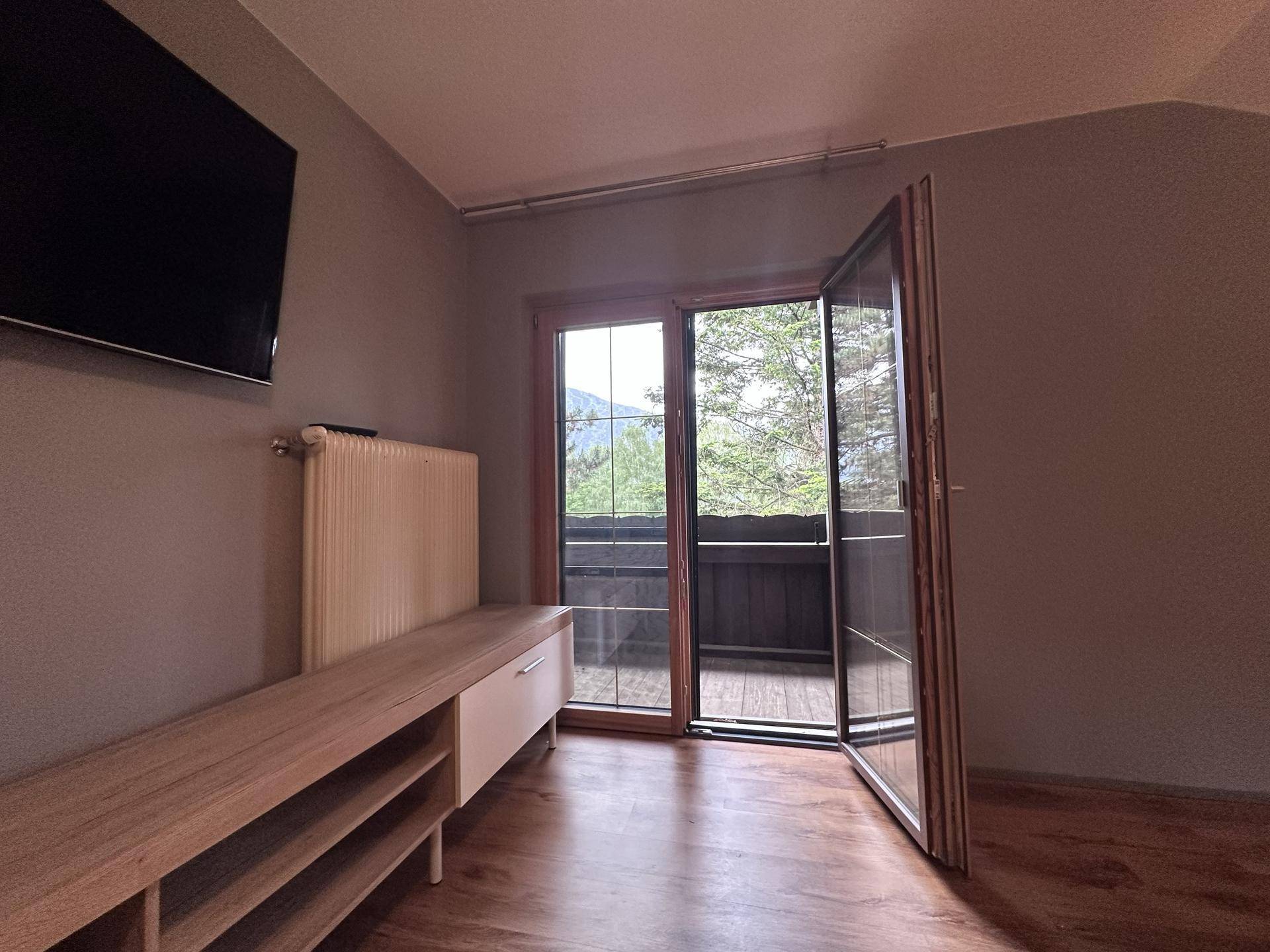 Schlafzimmer mit Balkonzugang, Holzlaminatboden und Blick auf die Berge.