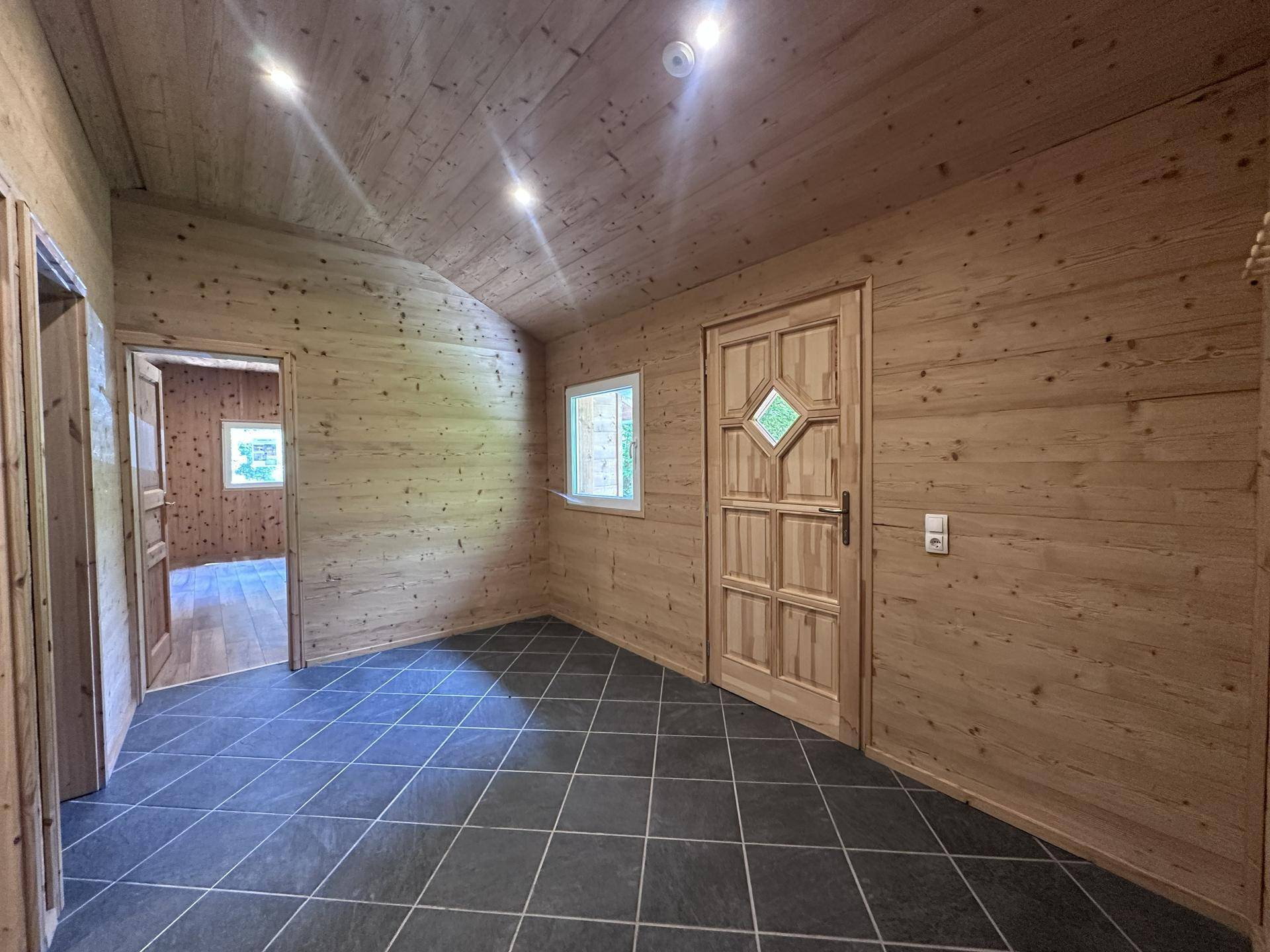 Eingangsbereich mit dunklen Fliesen, Holzvertäfelung und rustikaler Holztür.