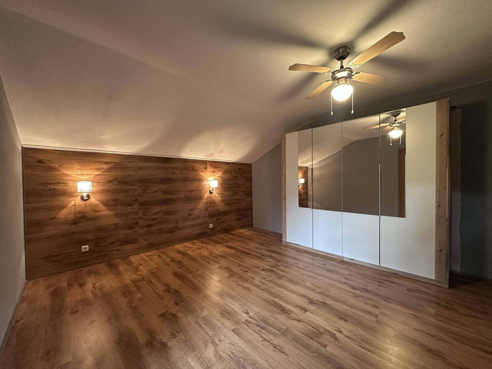 Helles Schlafzimmer mit Holzlaminatboden, Spiegelschränken und Deckenventilator.