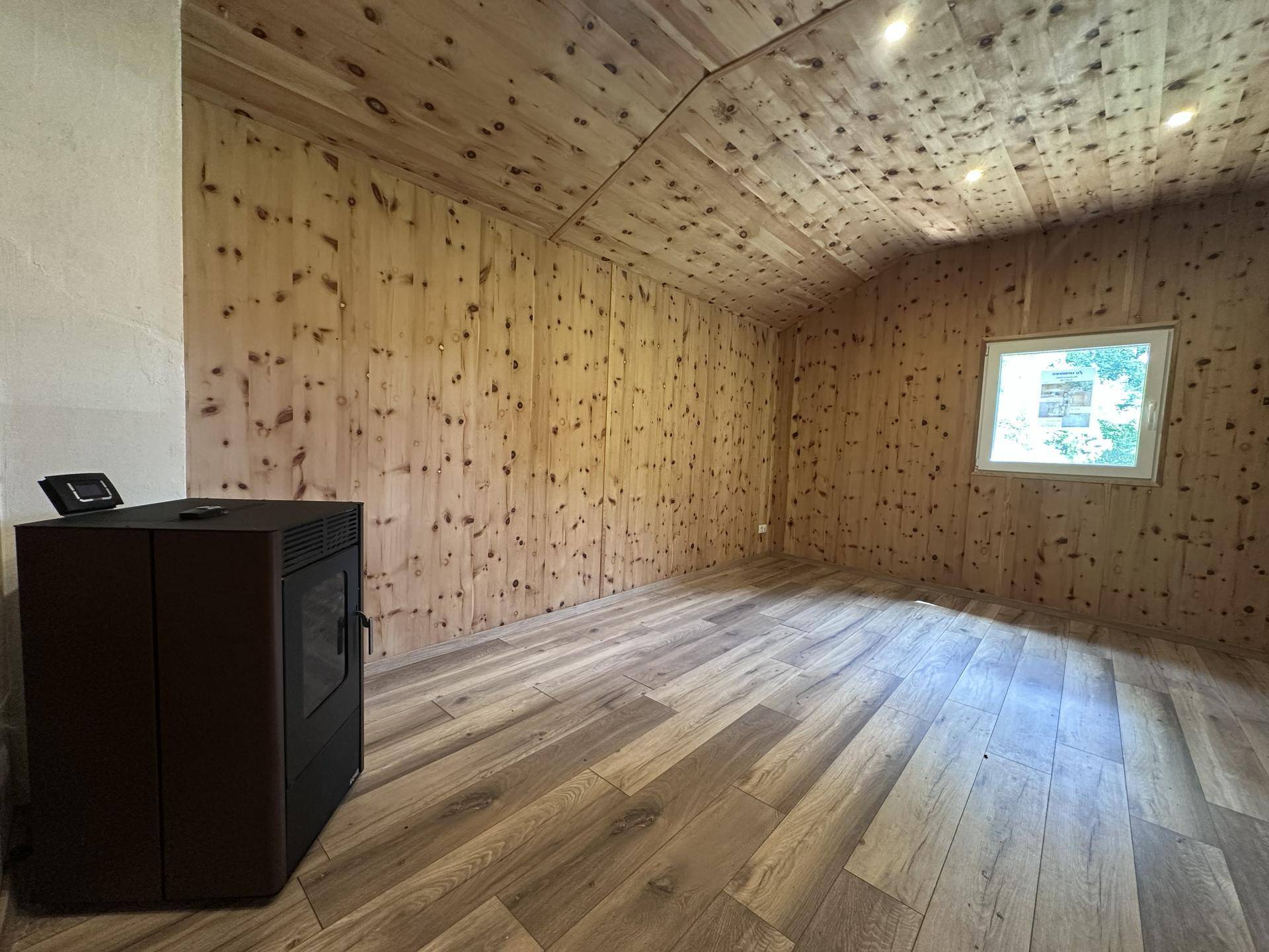 Helles Wohnzimmer mit Holzvertäfelung, modernem Pelletofen und Blick ins Grüne.