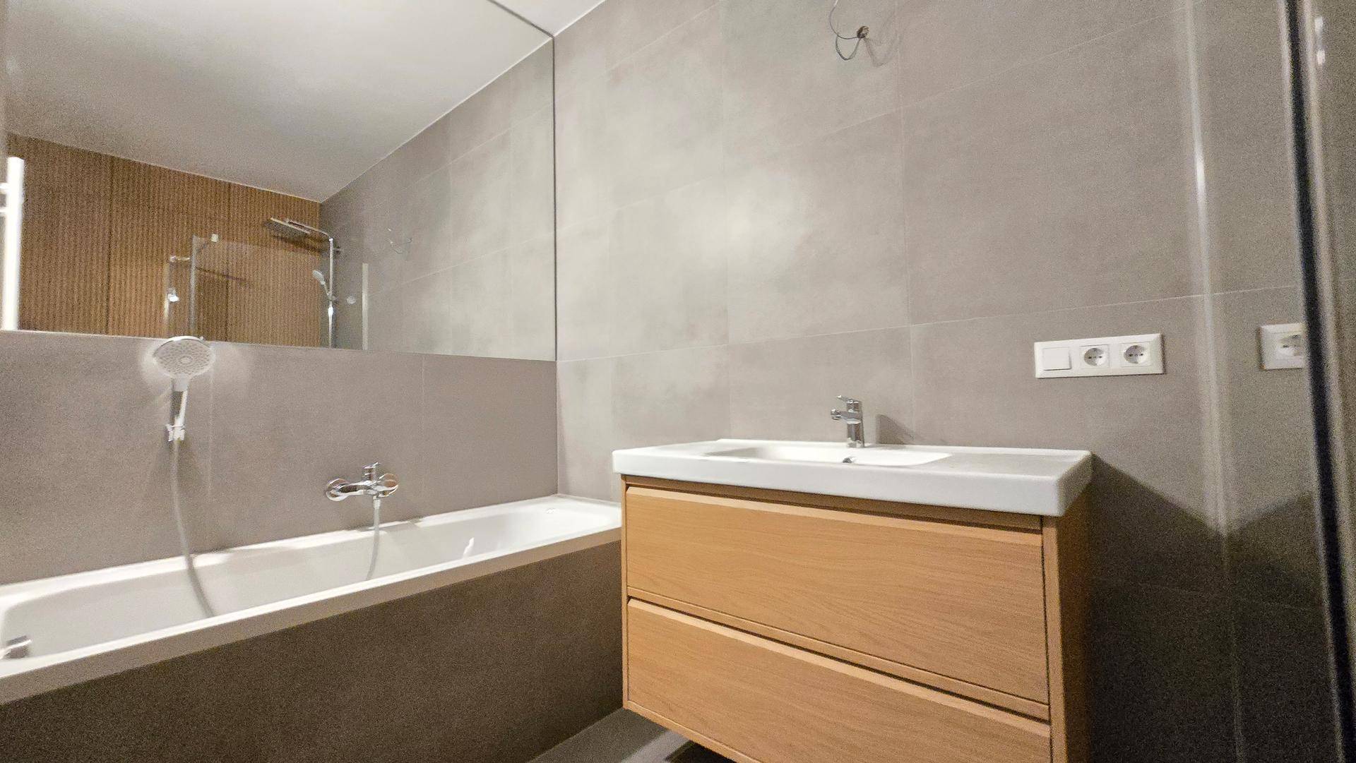 Zeitgemäßes Badezimmer mit Badewanne, Einzelwaschbecken und großem Spiegel über die gesamte Wand.
