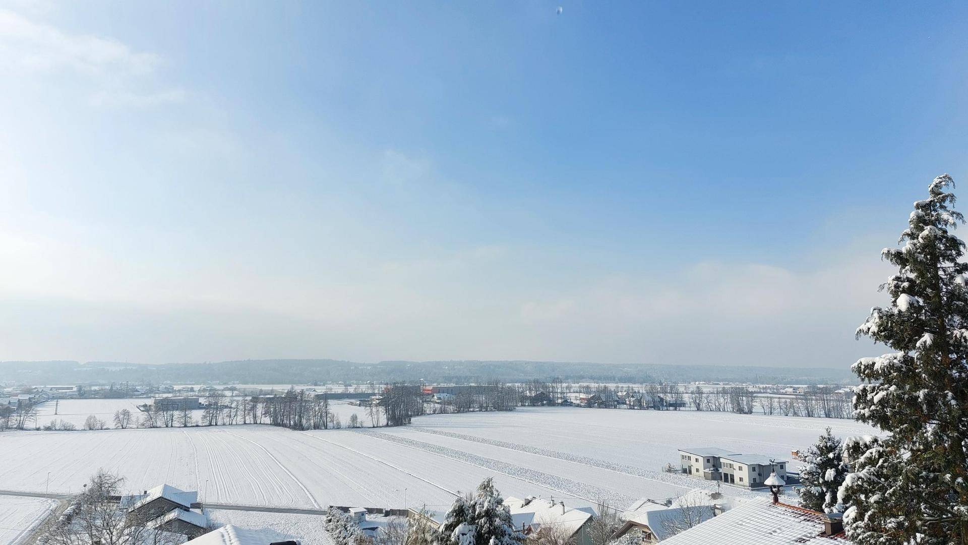 Winterlicher Panoramablick über eine verschneite Landschaft mit Häusern und Bäumen unter klarem Himmel.