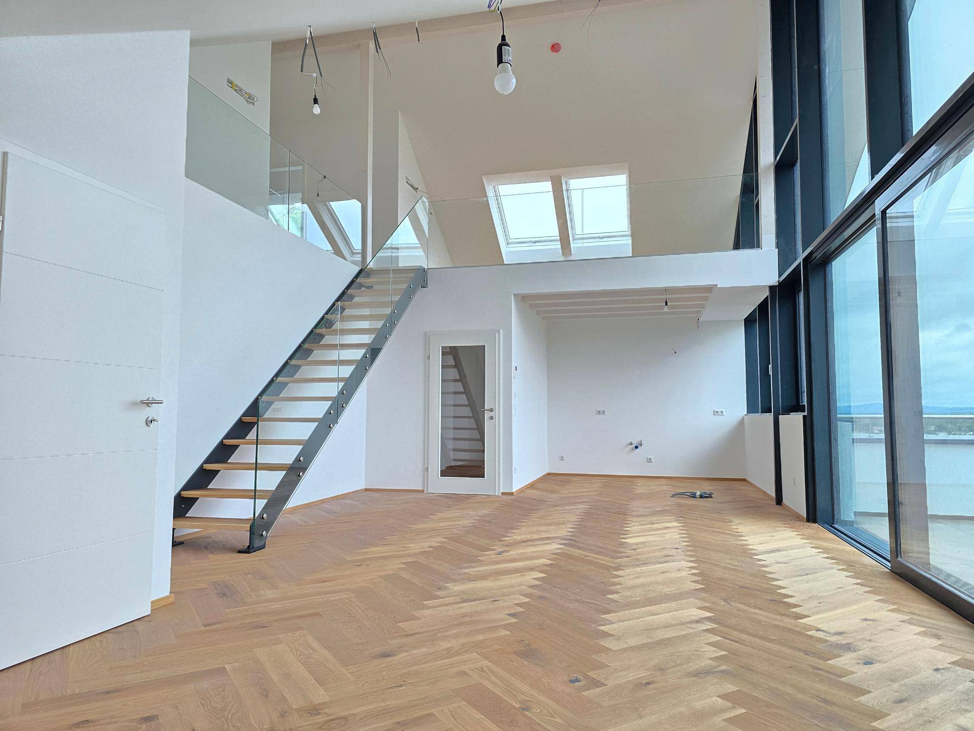 Geräumiges Wohnzimmer mit Fischgrätparkett, offener Galerie und viel Tageslicht durch Dachfenster.