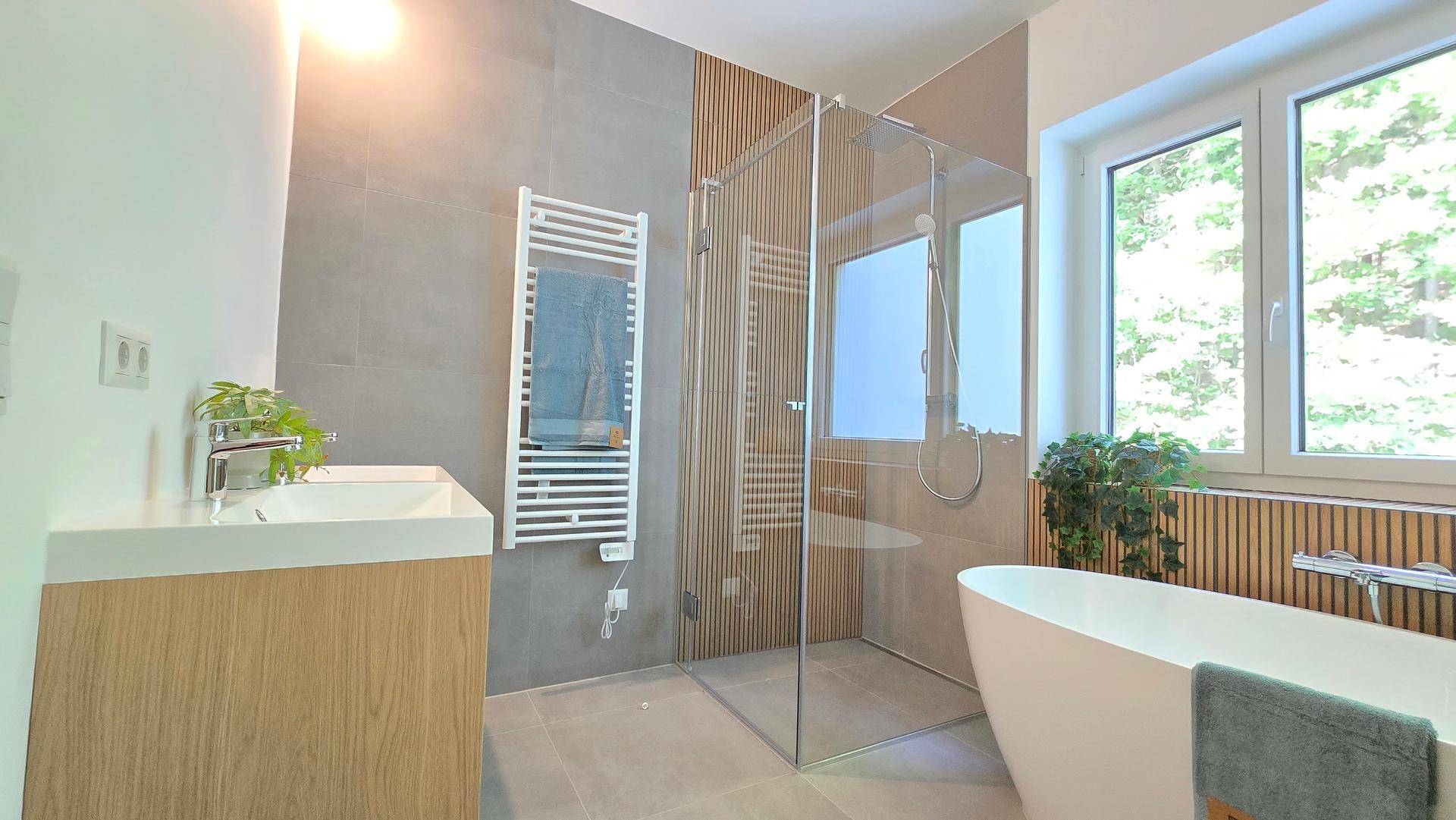 Modernes Badezimmer mit freistehender Badewanne, begehbarer Dusche und beheiztem Handtuchhalter an der Wand.
