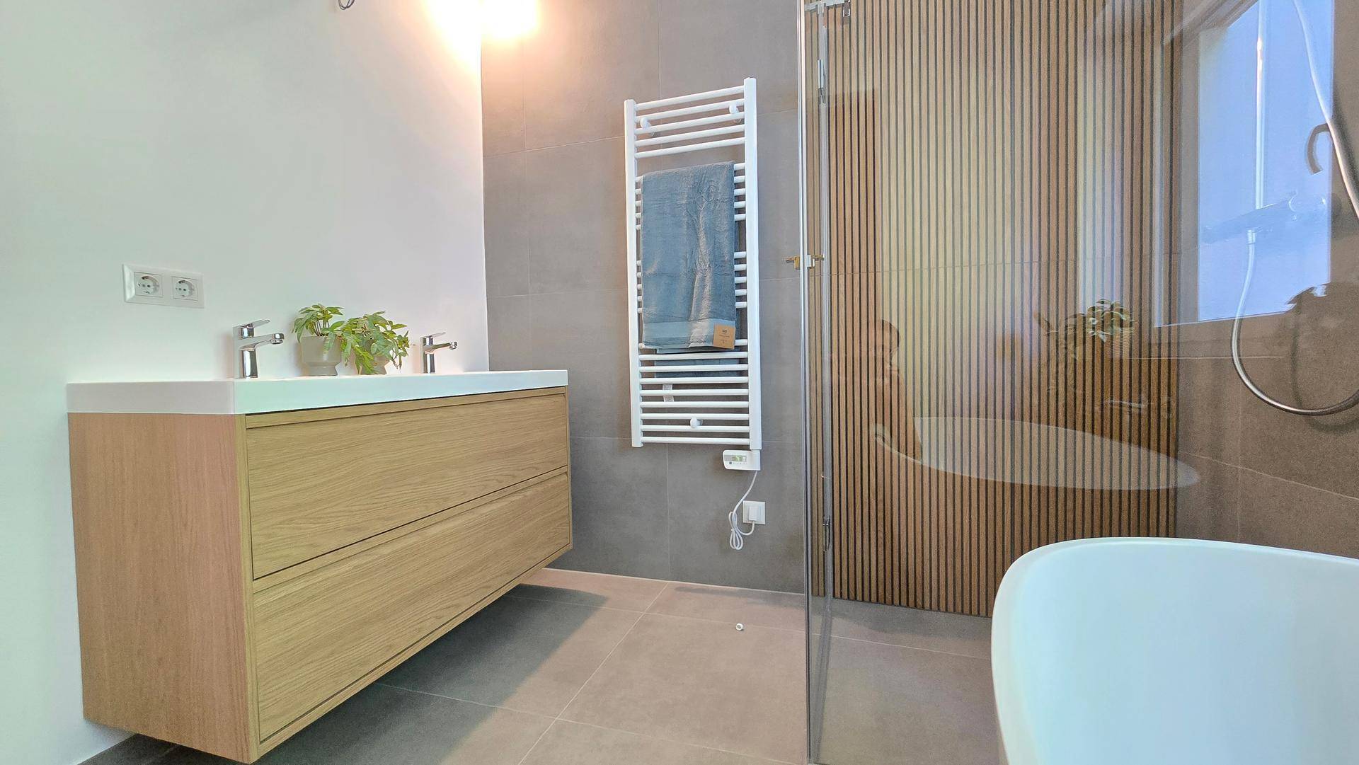 Modernes Badezimmer mit Doppelwaschbecken, Holzunterschrank und beheiztem Handtuchhalter an der Wand.