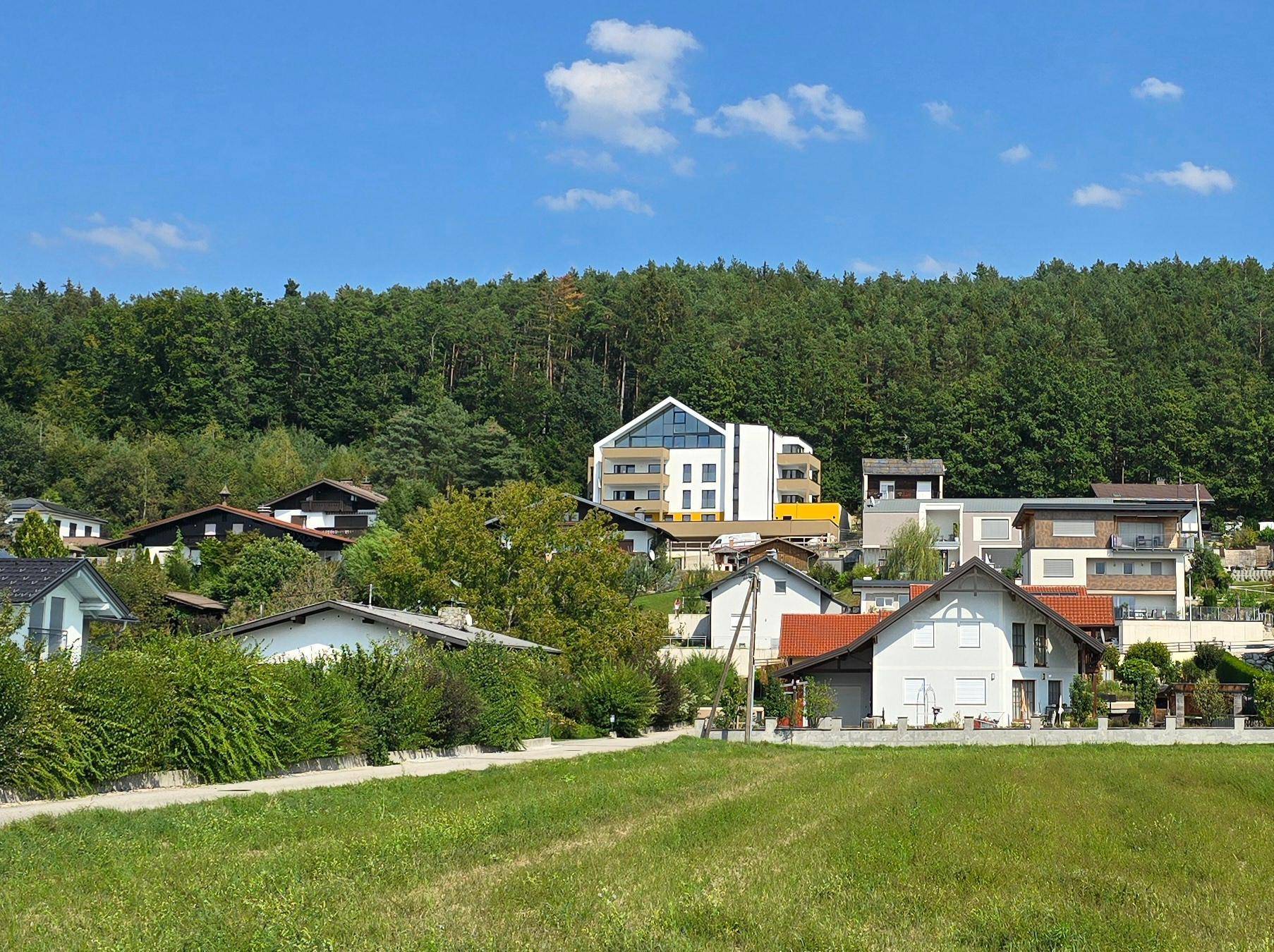 Wohnsiedlung in grüner Hügellandschaft mit Wald im Hintergrund und weitem Blick.