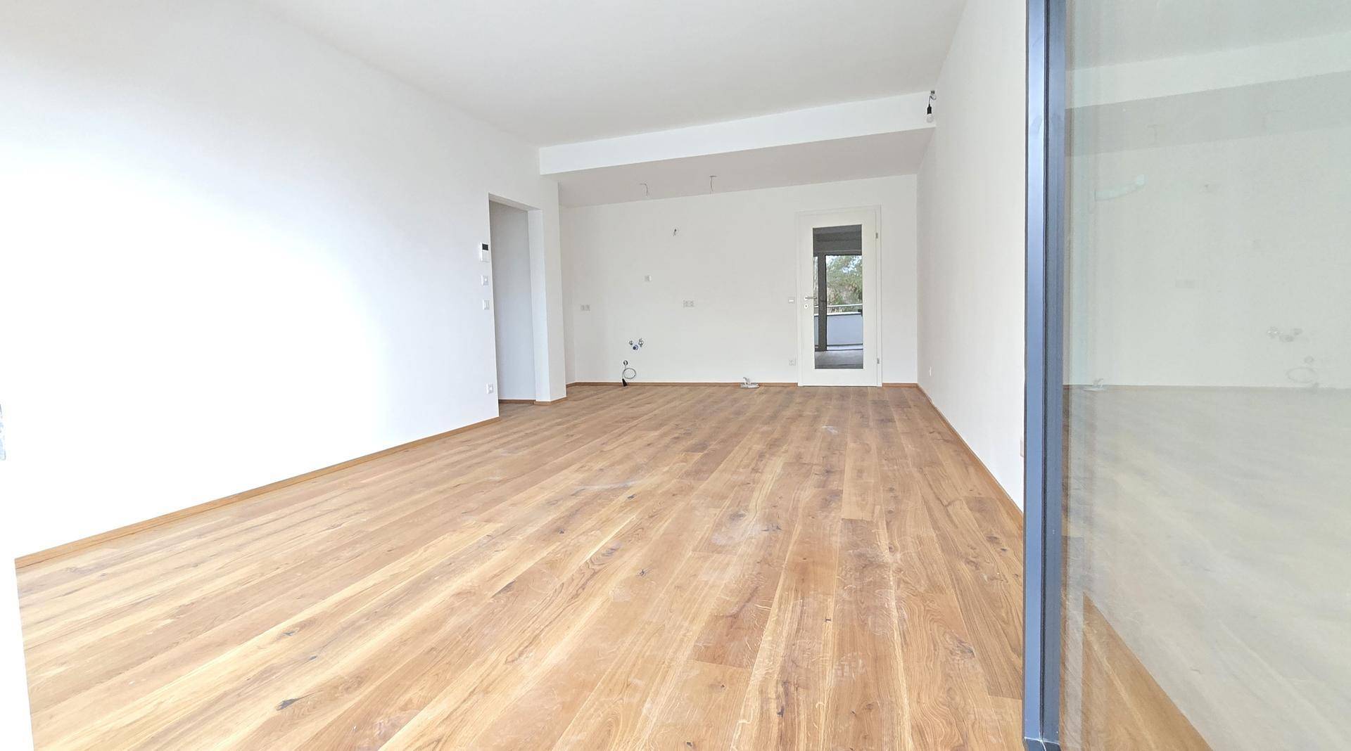 Geräumiger, unmöblierter Raum mit hellem Holzparkett und Zugang zu einem weiteren Bereich.