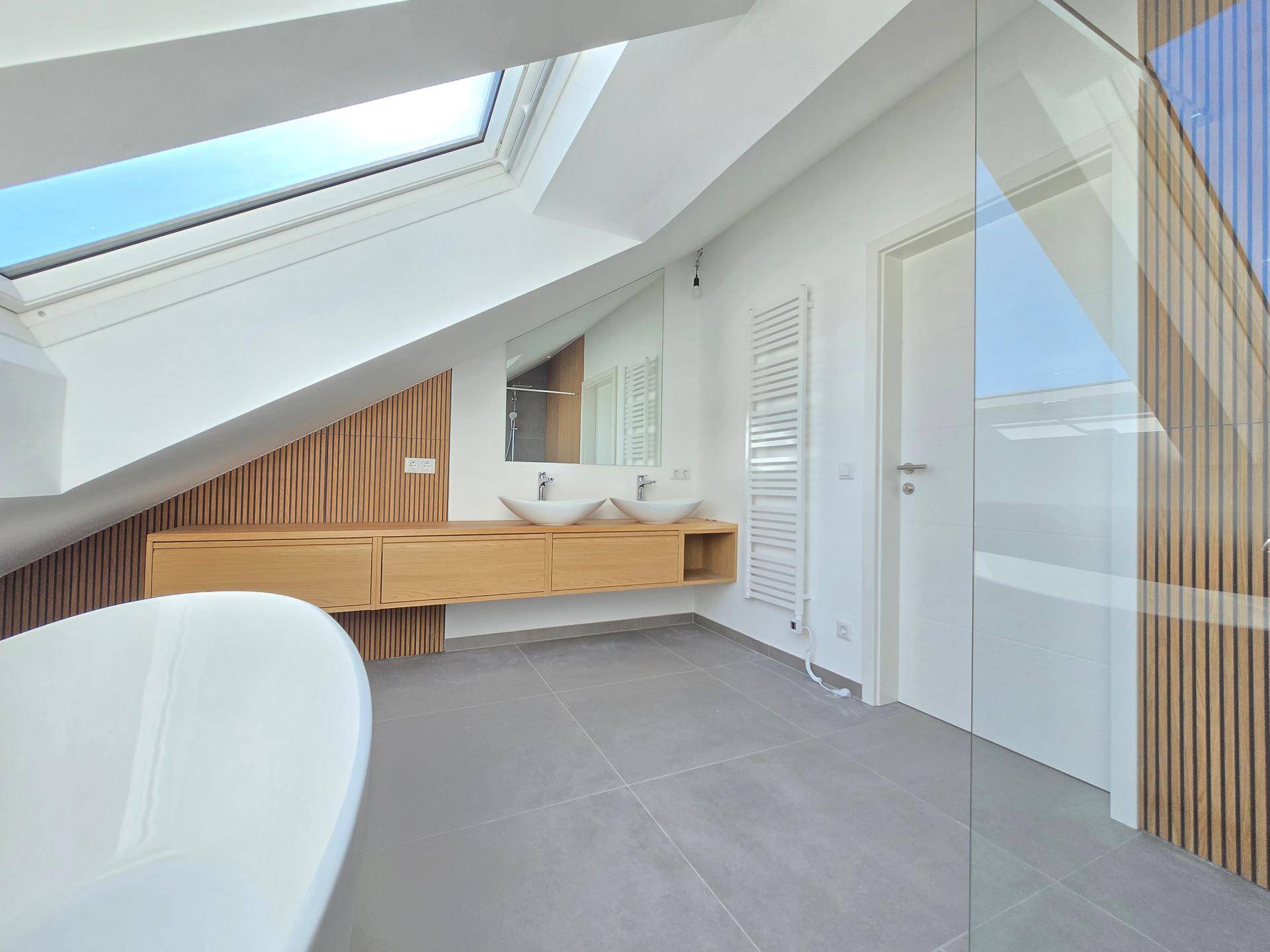 Modernes Dachgeschossbad mit Doppelwaschbecken, freistehender Badewanne und großem Dachfenster.