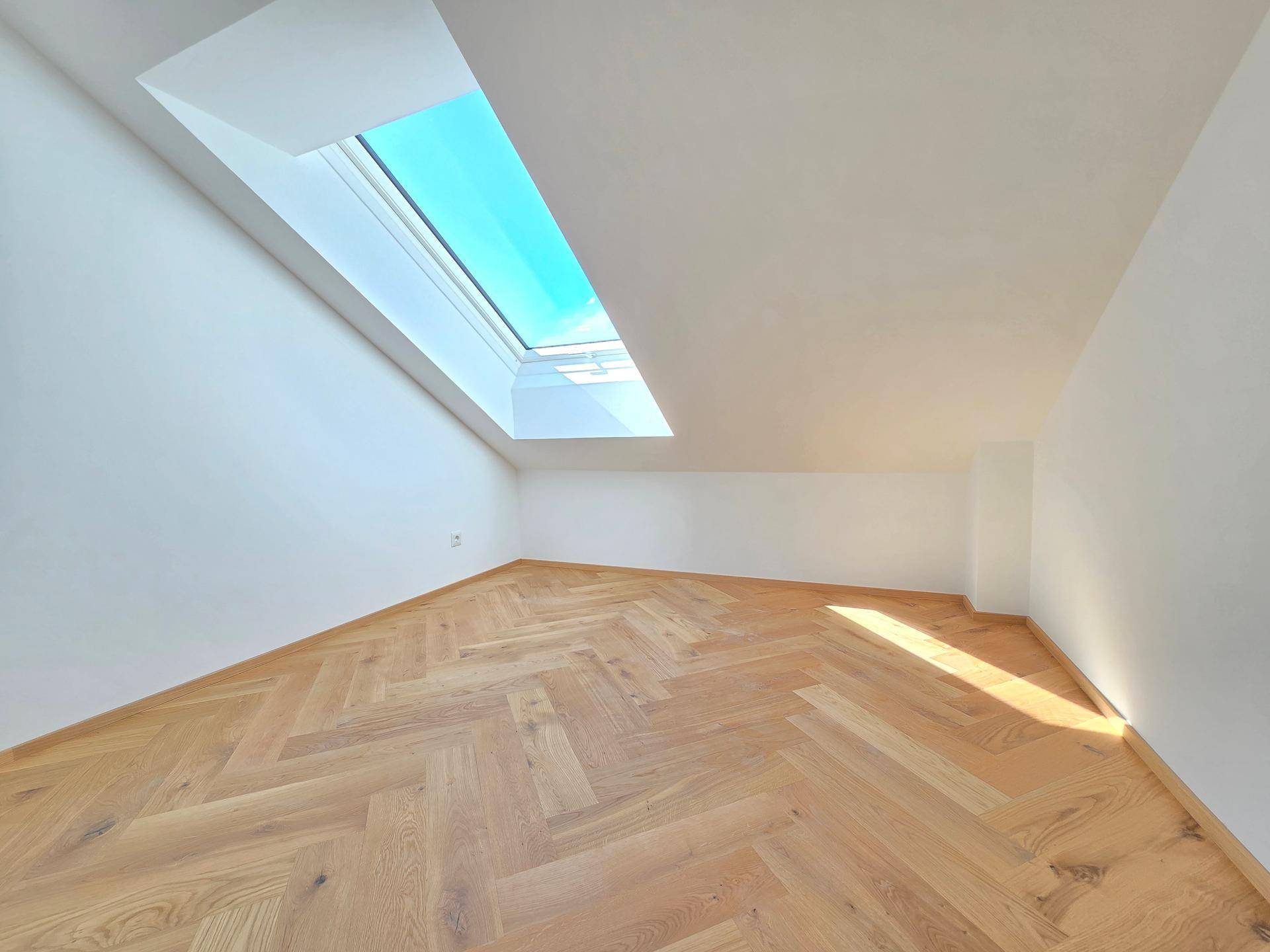 Helles Dachgeschosszimmer mit Fischgrätparkett und großem Dachfenster, das viel Sonnenlicht spendet.