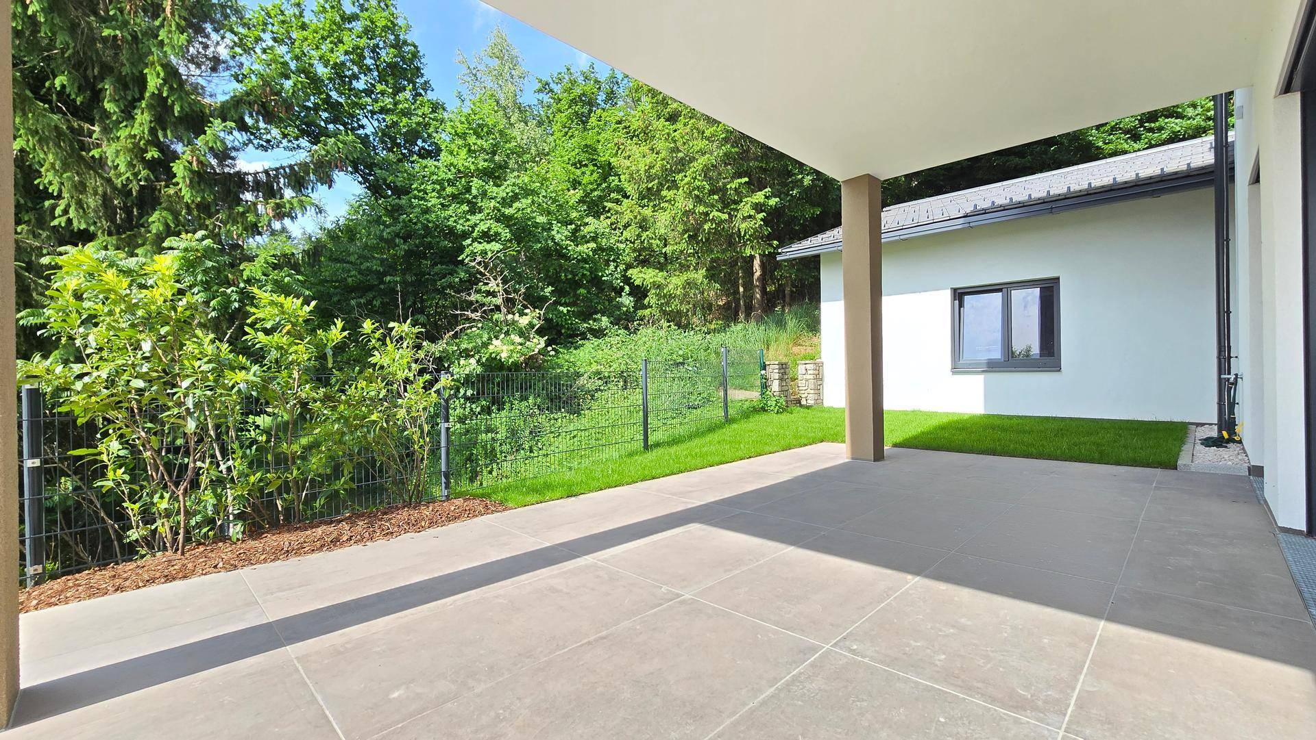 Überdachte Terrasse mit Fliesenboden und Blick auf den Gartenbereich und das Nebengebäude.