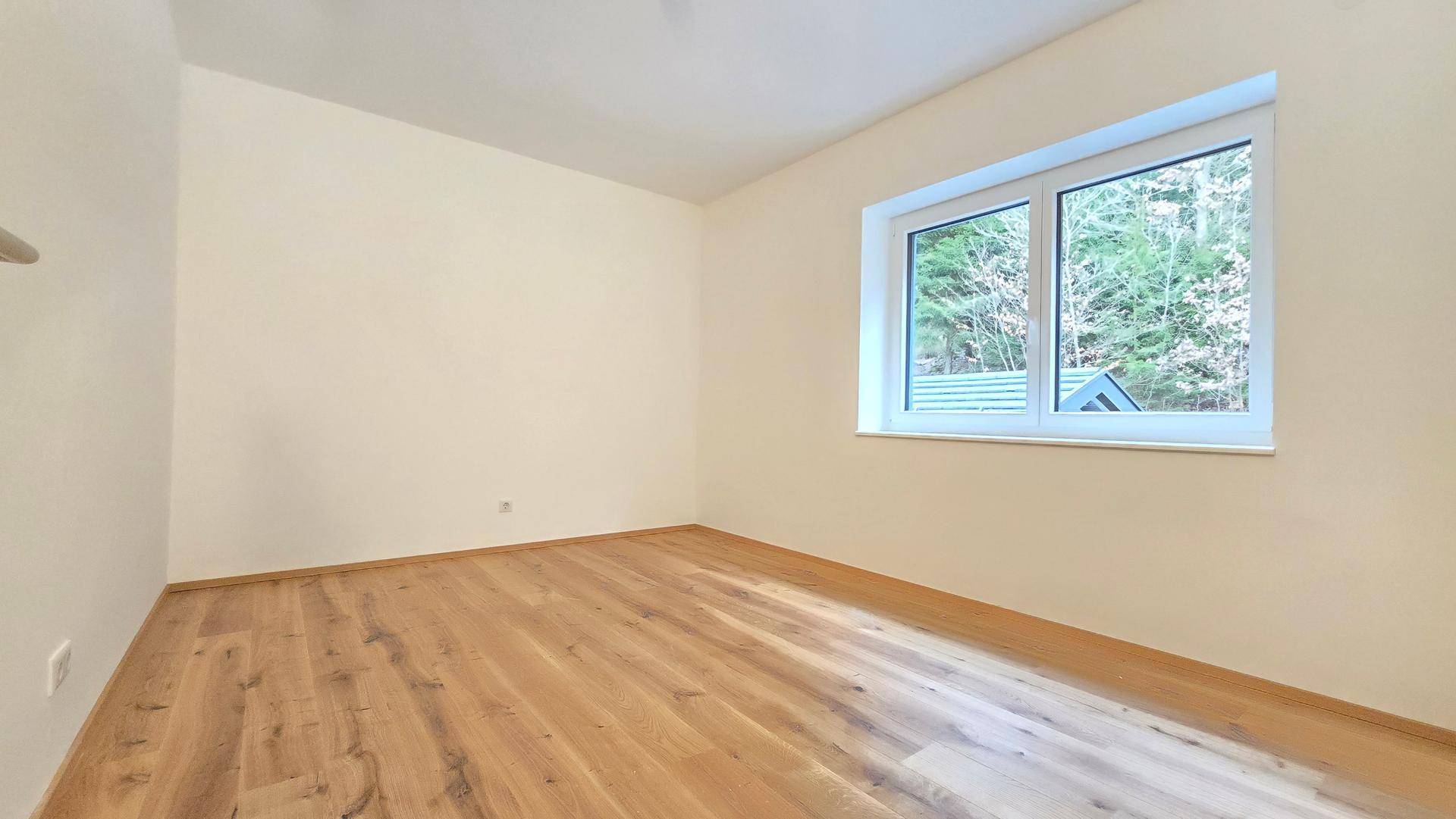Helles Schlafzimmer mit Blick ins Grüne, hellem Parkettboden und cremefarbenen Wänden.