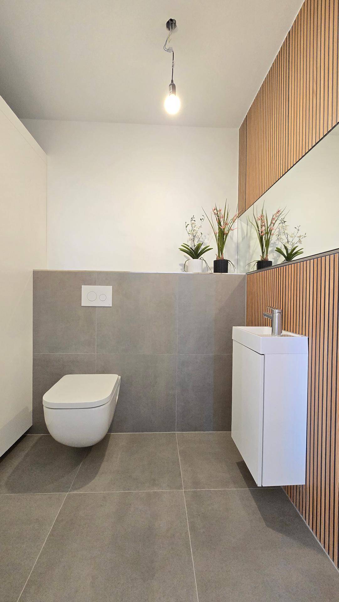 Modernes Gäste-WC mit wandhängender Toilette, kleinem Waschbecken und Holzlamellenwand.