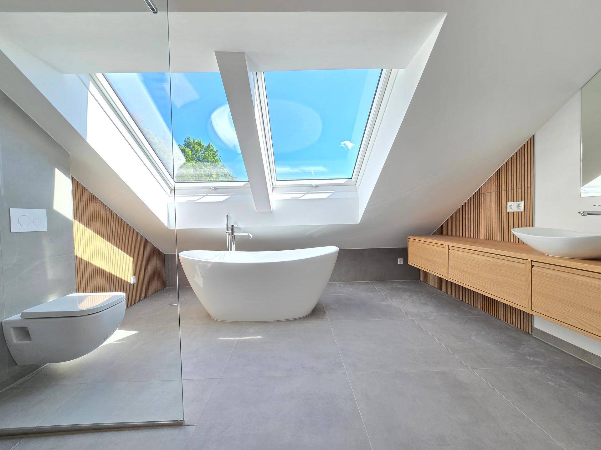 Modernes Dachgeschossbad mit freistehender Badewanne, Wand-WC und großen Dachfenstern für viel Licht.