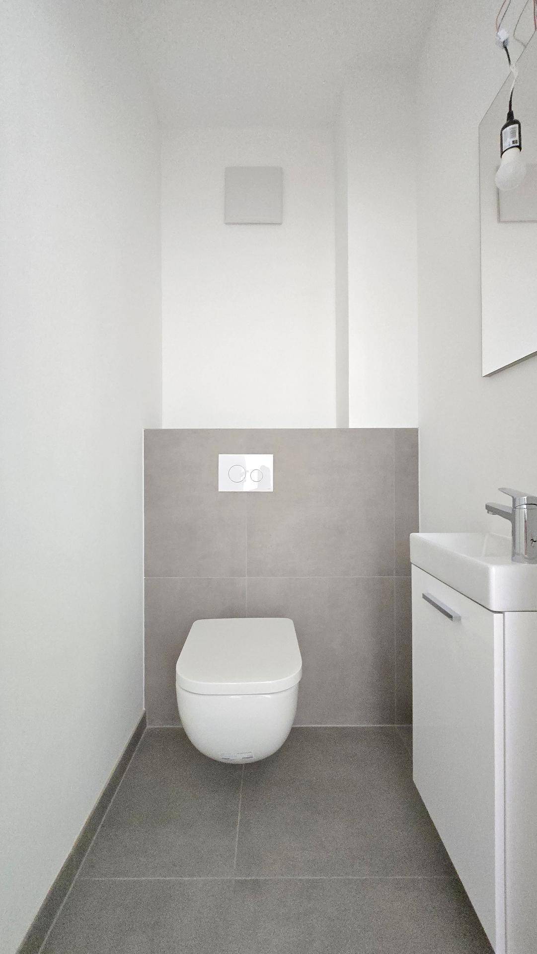 Kompaktes Gäste-WC mit wandhängender Toilette und kleinem Waschbecken, modern gefliest.