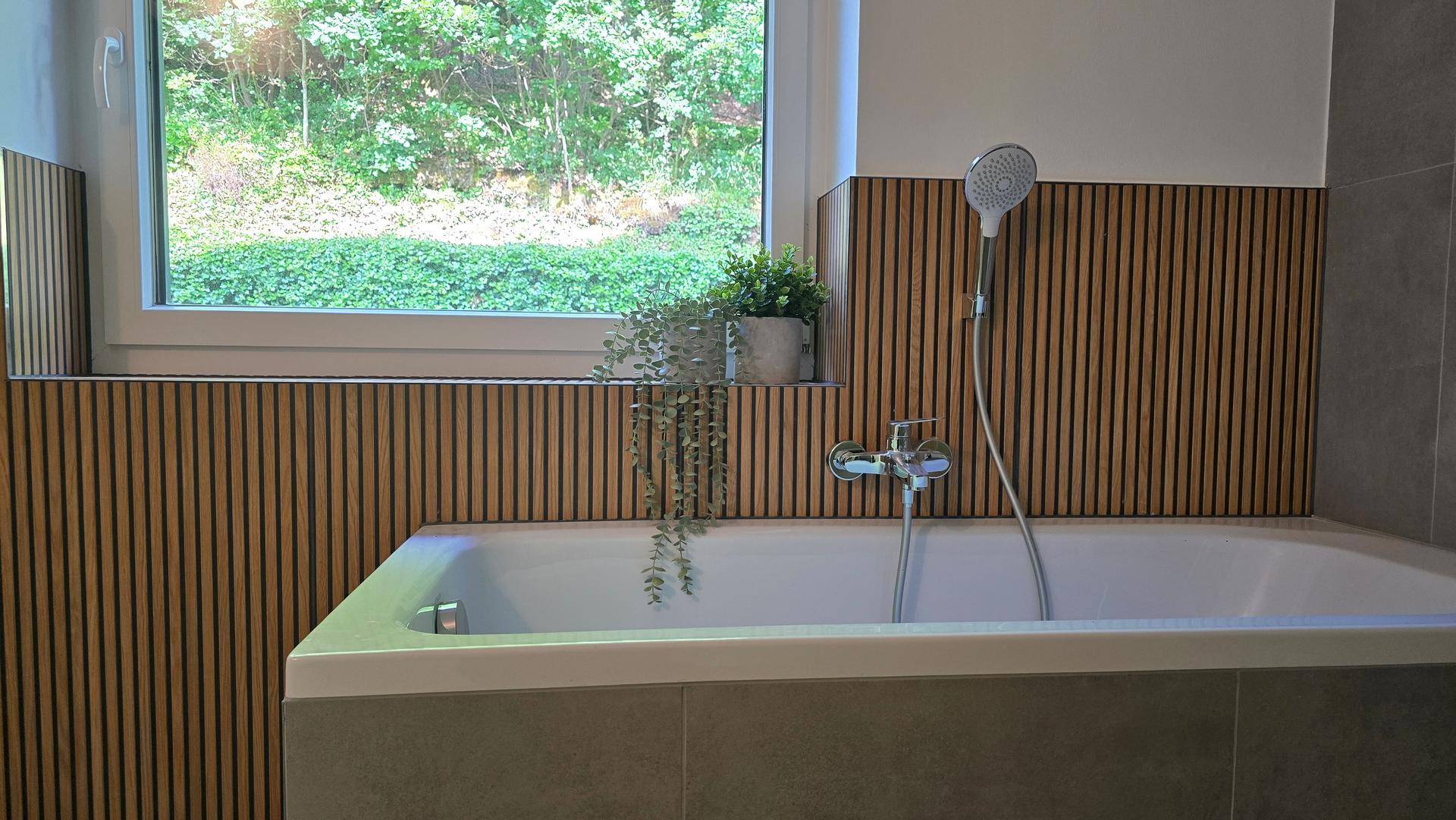 Detailansicht der Badewanne im modernen Badezimmer mit Holzlamellenwand und Fenster.