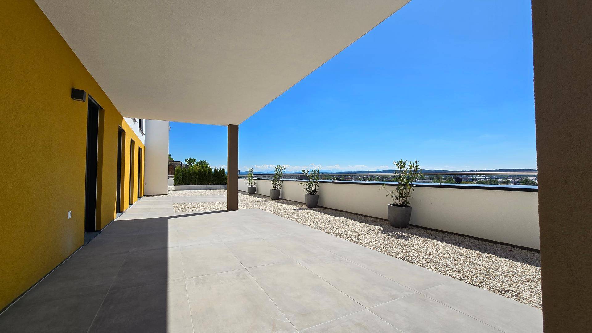 Geräumige, unmöblierte Terrasse mit Fliesenboden und Kiesbereich, bietet weite Aussicht.
