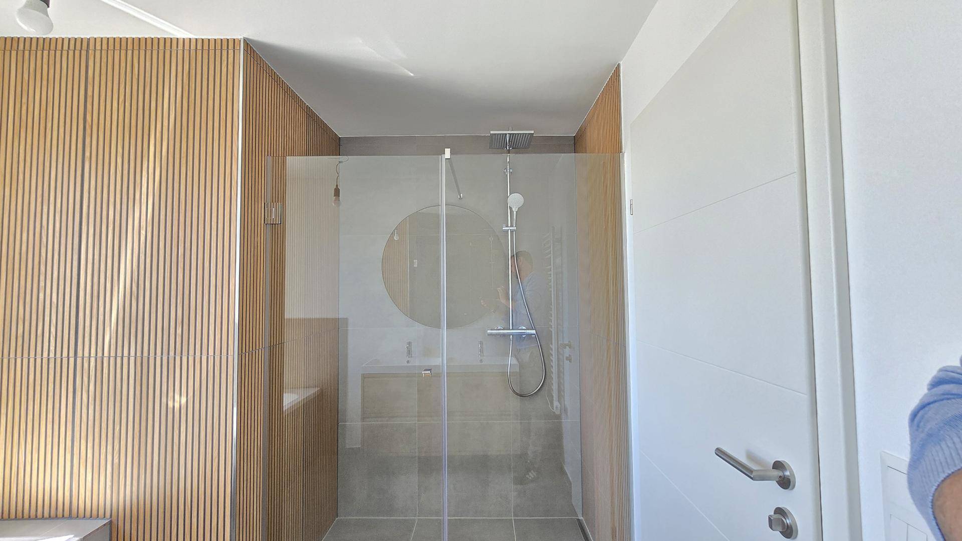 Modernes Badezimmer mit begehbarer Dusche, Glasabtrennung und stilvollen Holzlamellenwänden.