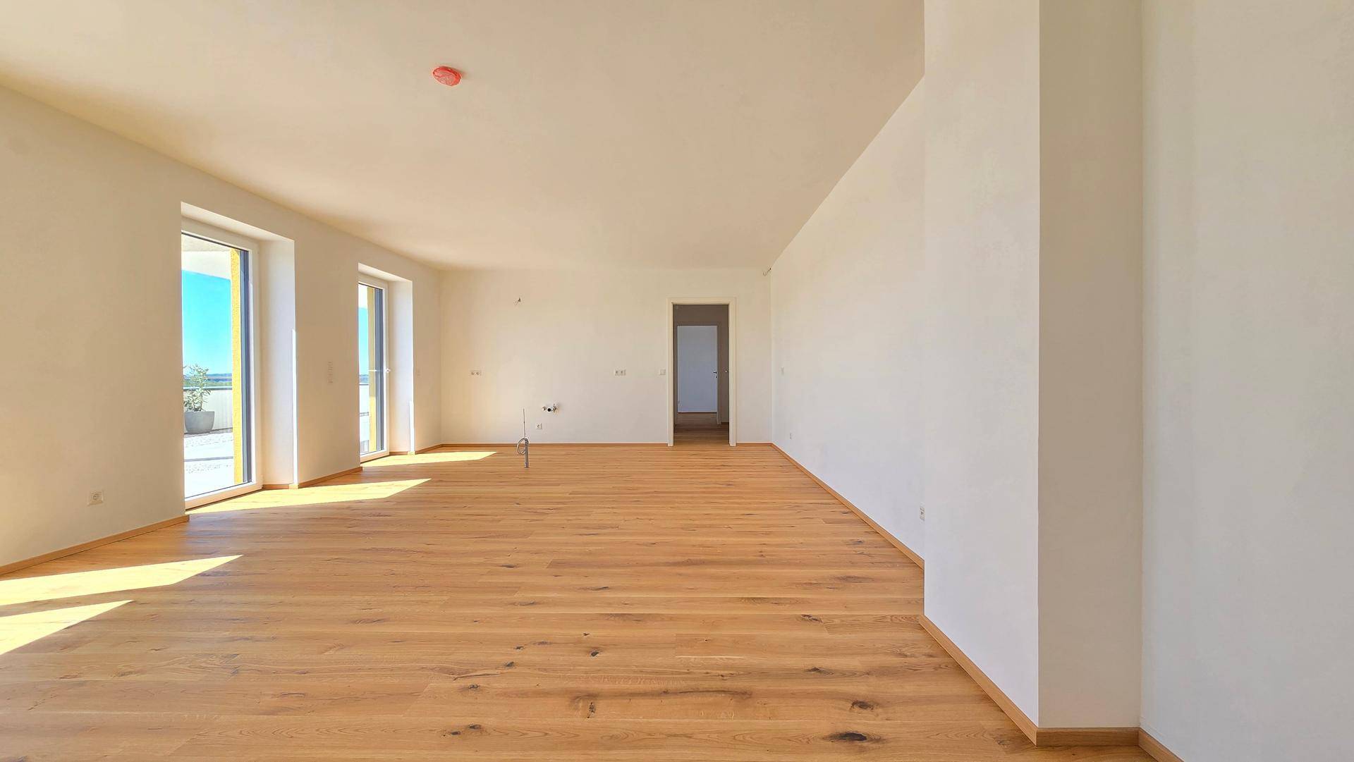 Heller, leerer Wohnraum mit hochwertigem Holzplankenboden und großen Fenstern zum Außenbereich.