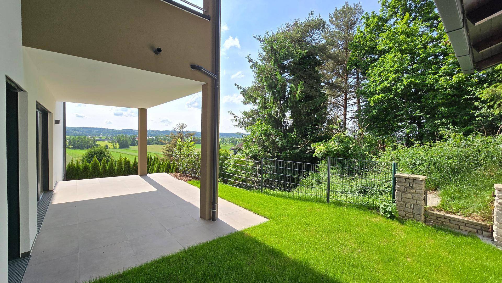 Überdachte Terrasse mit Rasenfläche und weitem Blick auf die umliegende grüne Landschaft.