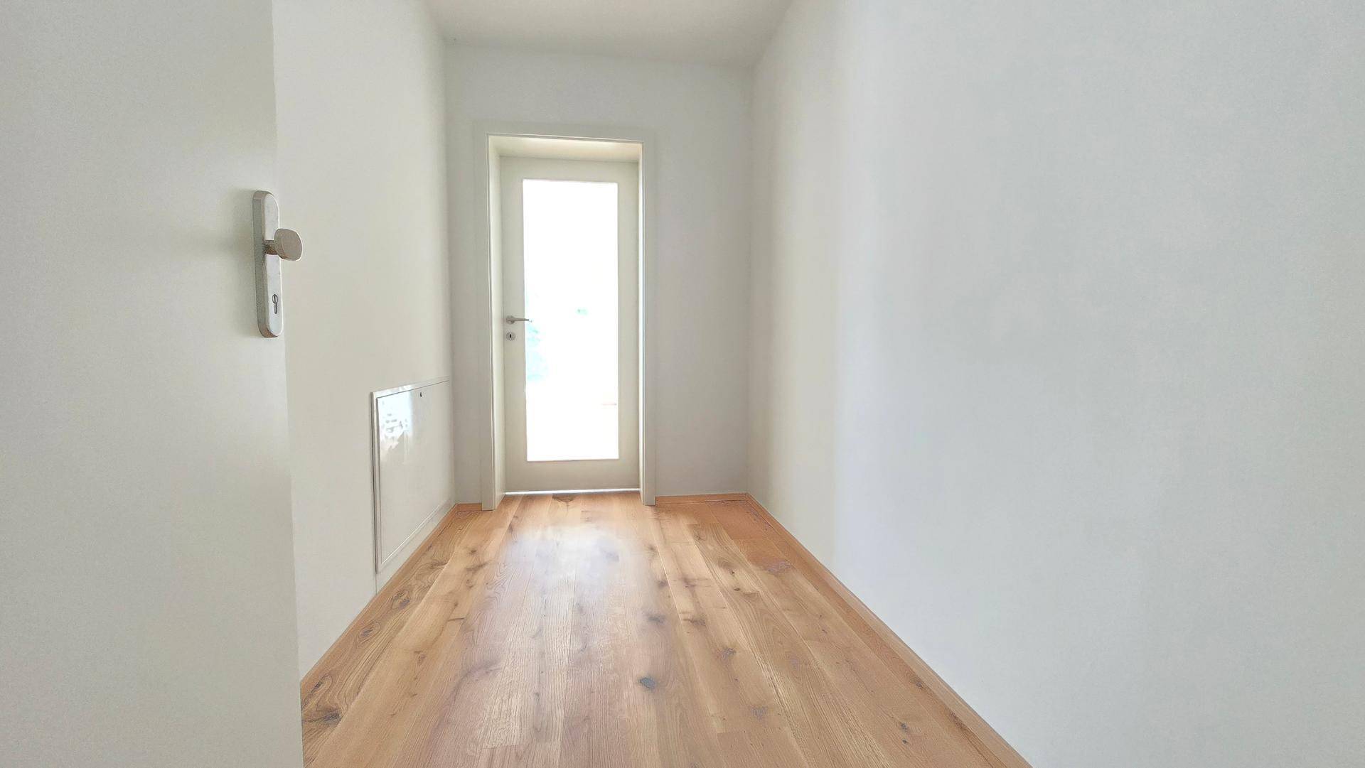 Heller Flur mit Holzboden und weiß gestrichenen Wänden, führt zu weiteren Räumen.