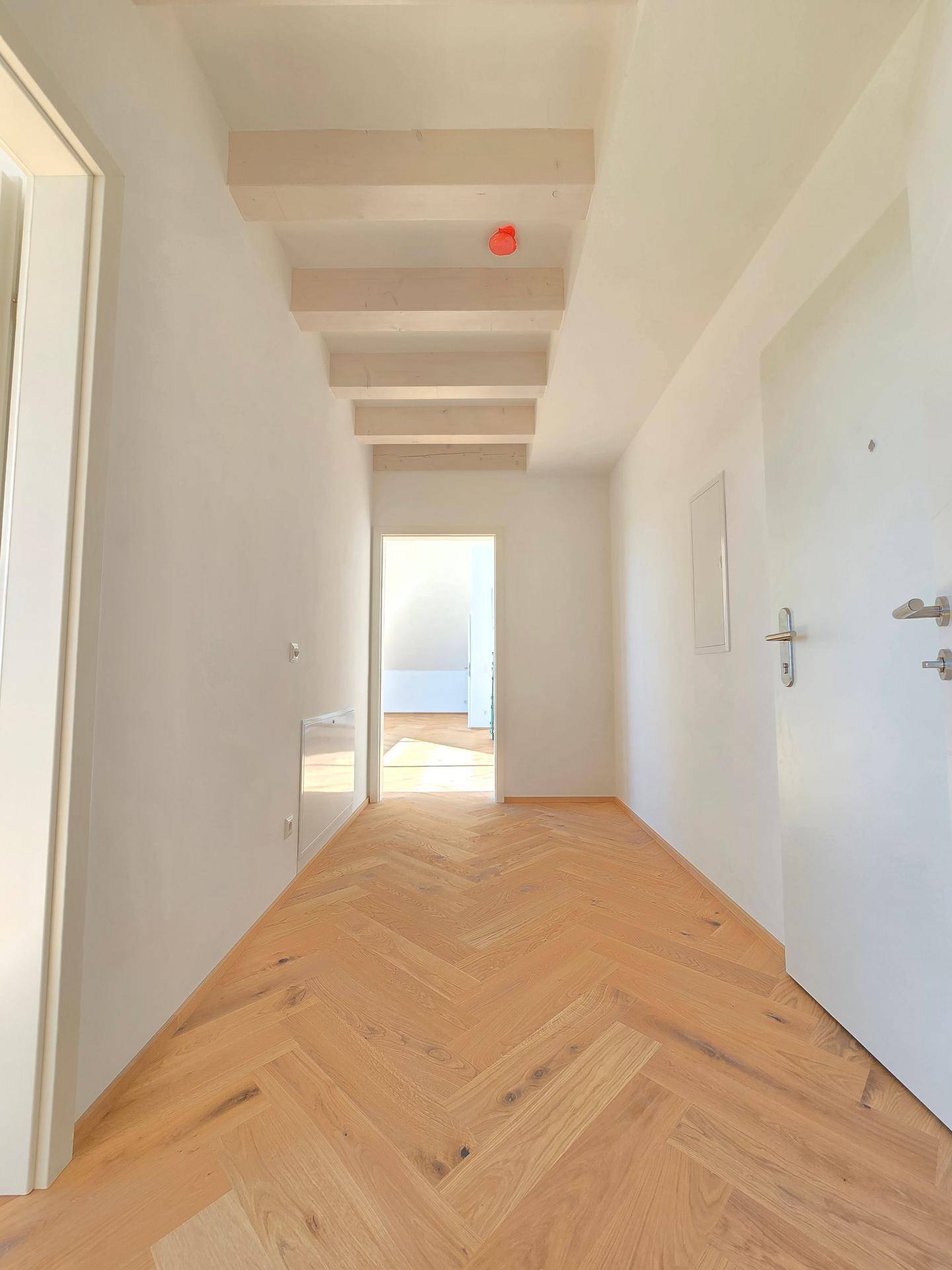 Heller Flur mit Fischgrätparkett und sichtbaren Holzbalken an der Decke, führt zu weiteren Räumen.