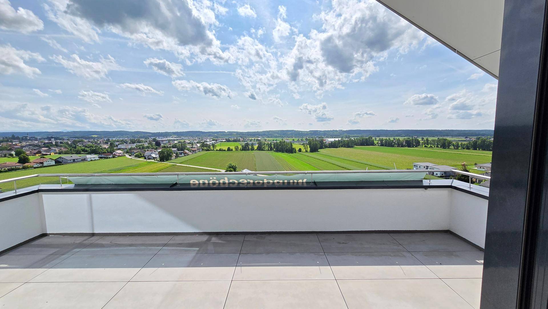 Geräumige Terrasse mit weitem Blick über grüne Felder und die umliegende Landschaft unter blauem Himmel.