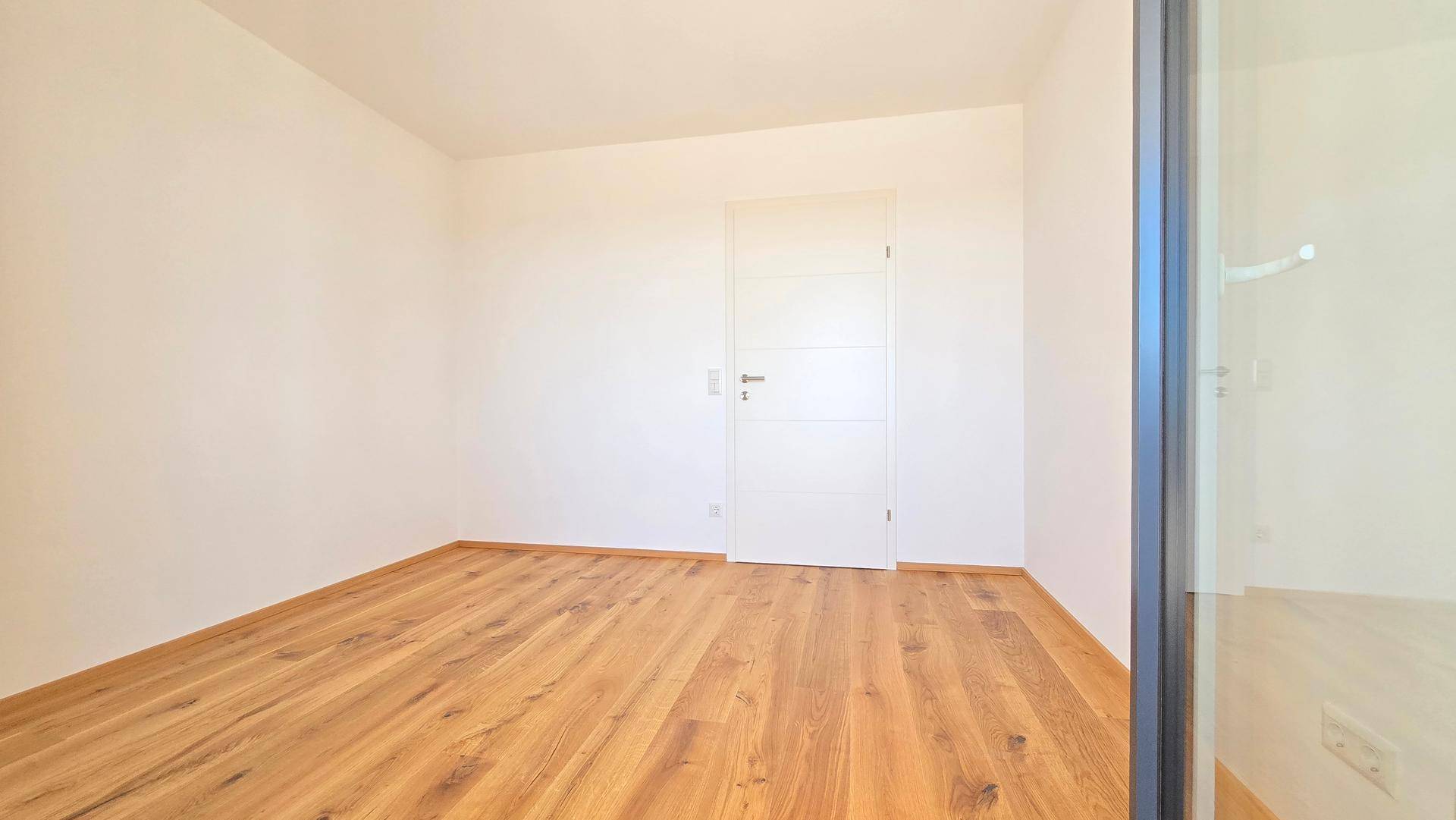 Helles, unmöbliertes Zimmer mit Holzplankenboden und einer modernen weißen Innentür.