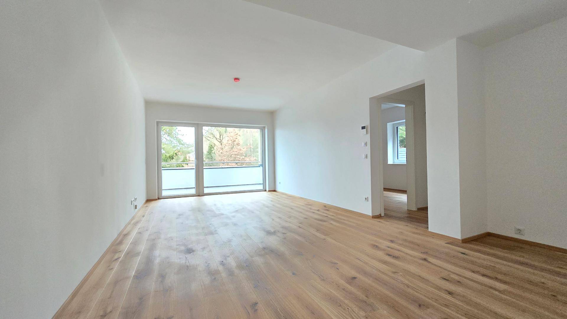 Heller, leerer Wohnraum mit großen Fenstern und neu verlegtem Holzparkettboden.
