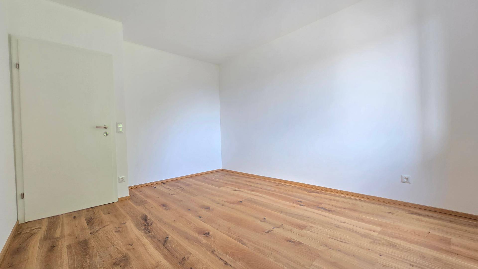 Heller Raum mit Holzboden und weißer Tür, ideal als Schlafzimmer oder Büro, bereit zur individuellen Gestaltung.