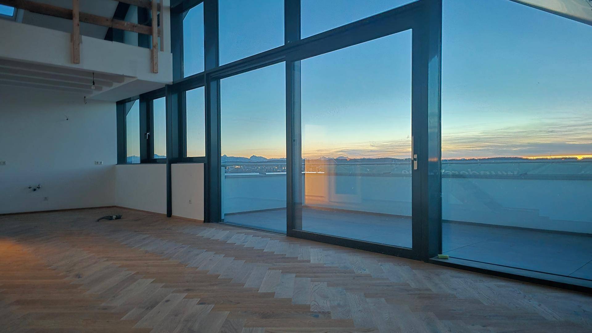 Geräumiges Wohnzimmer mit Fischgrätparkett und großen Fensterfronten, die einen weiten Blick bieten.