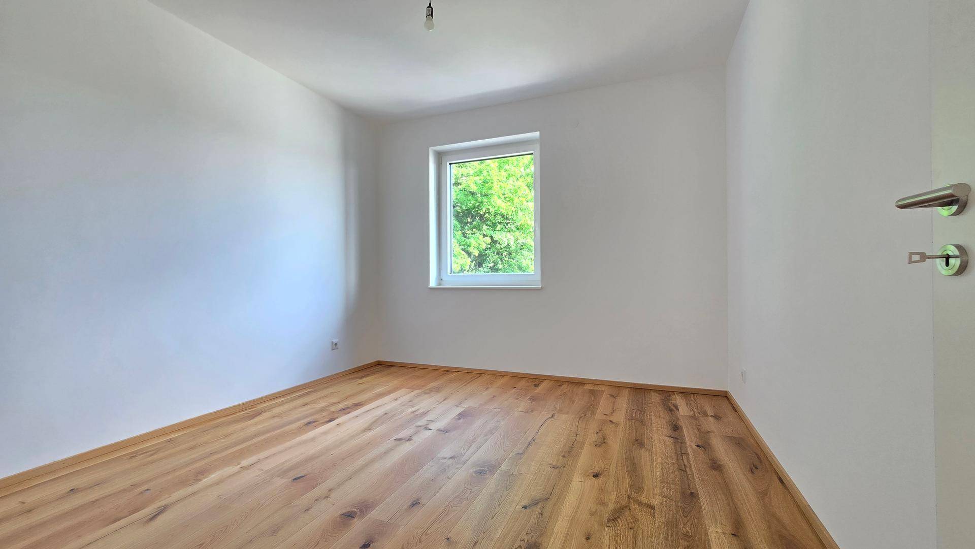 Geräumiges Schlafzimmer mit Holzboden und einem Fenster, das viel Tageslicht hereinlässt und Grünblick bietet.