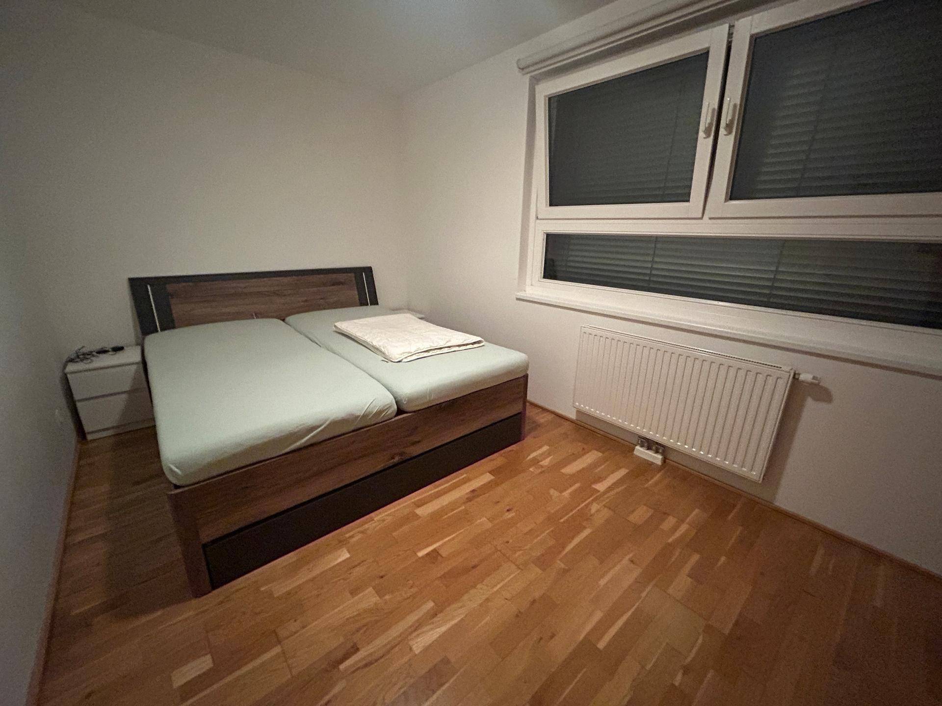 Gemütliches Schlafzimmer mit Doppelbett, Holzparkettboden und Fenster mit Jalousien.