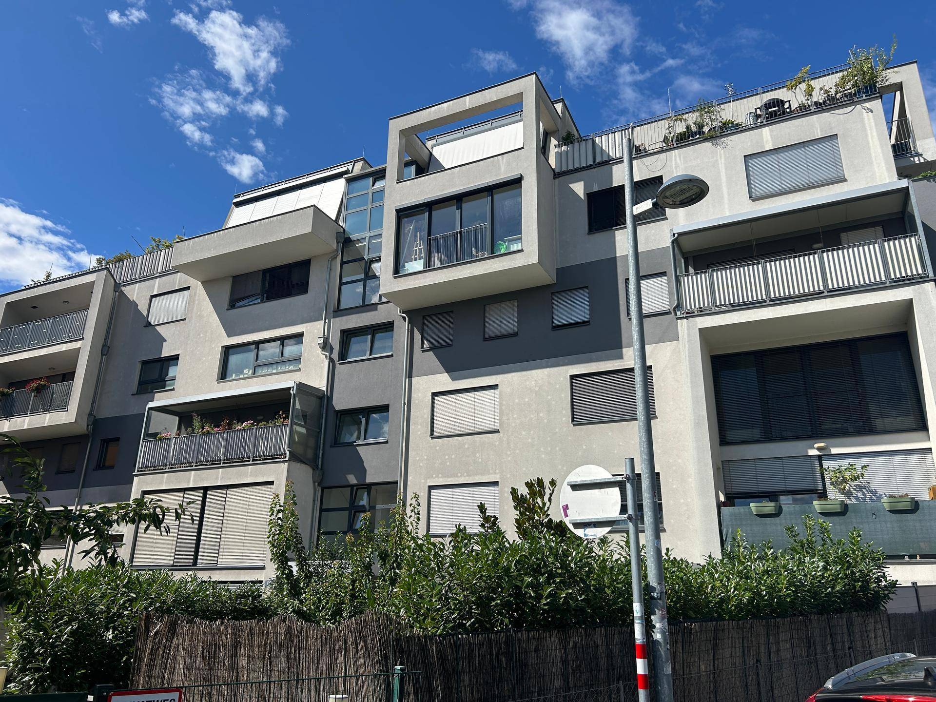Ansicht der modernen Wohnanlage mit gestuften Balkonen und Dachterrassen unter strahlend blauem Himmel.