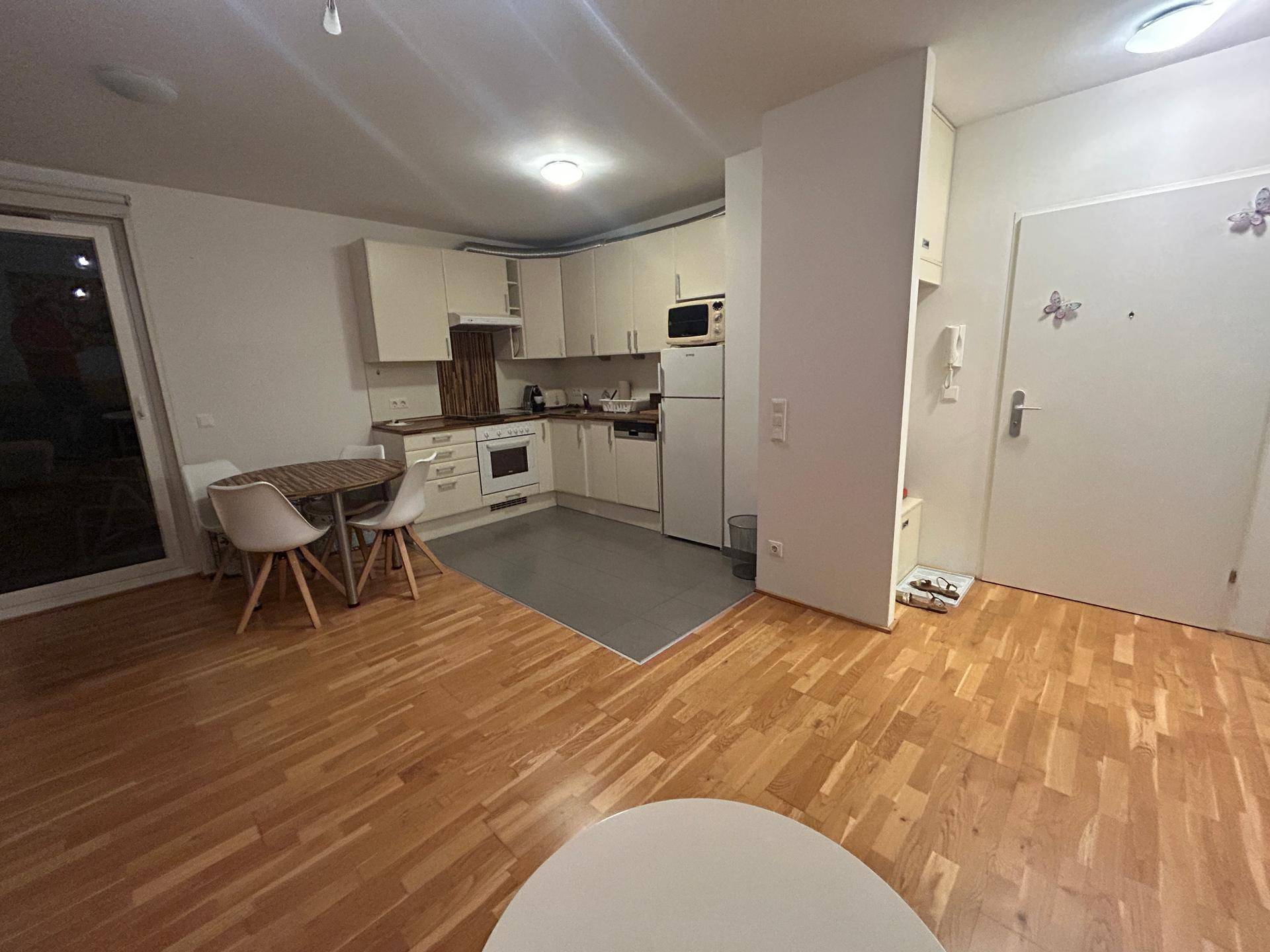 Funktionale Küche mit weißen Schränken und Essbereich, offen zum Wohnbereich mit Holzparkettboden.