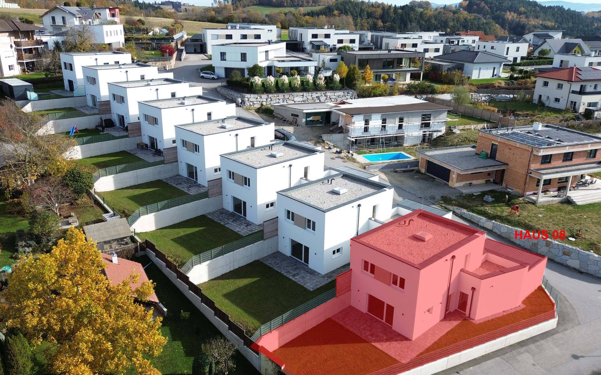 Luftaufnahme einer modernen Wohnsiedlung mit mehreren Häusern und Gärten in hügeliger Landschaft.
