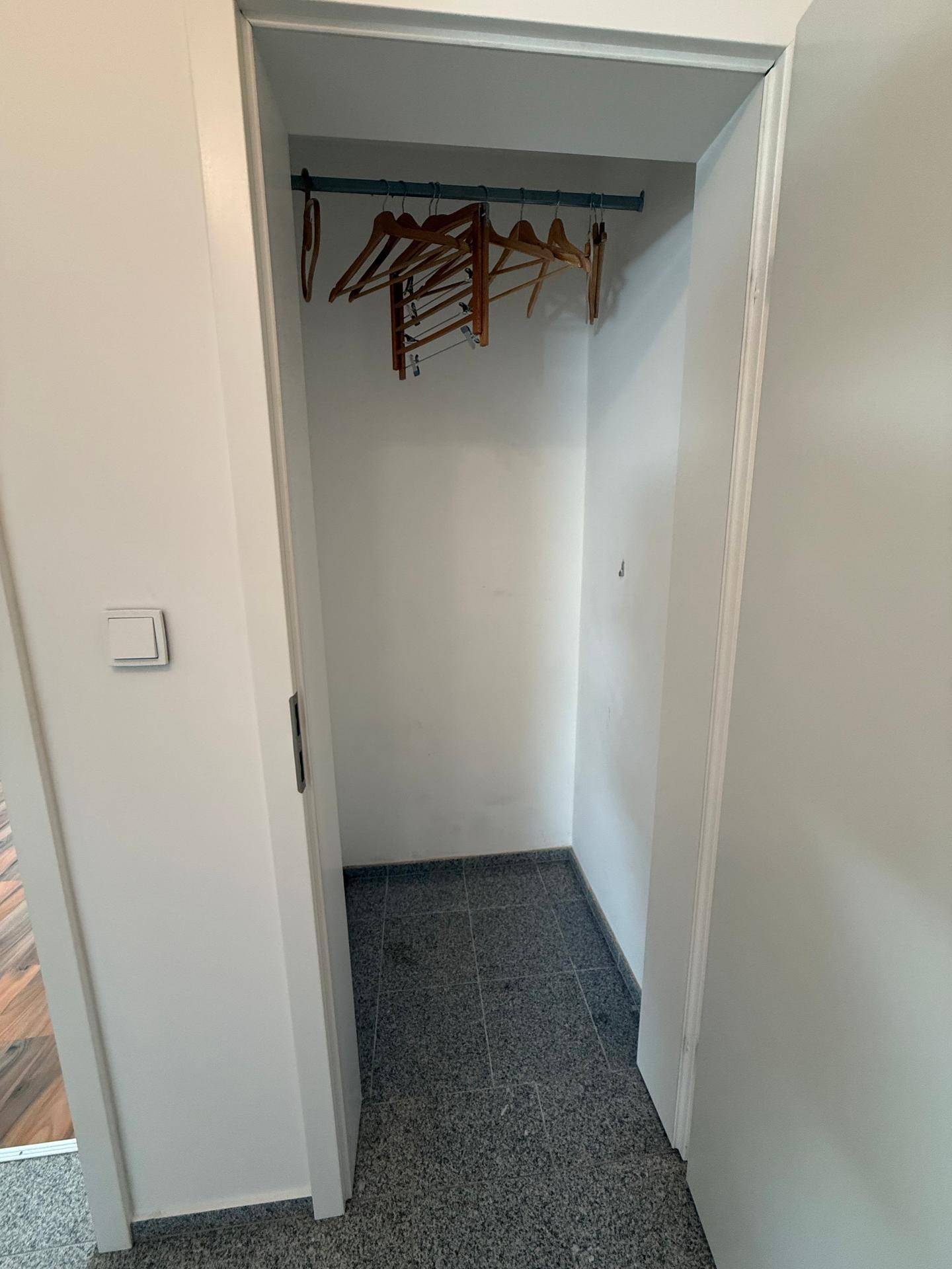 Kleiner Abstellraum mit Kleiderstange und Fliesenboden.