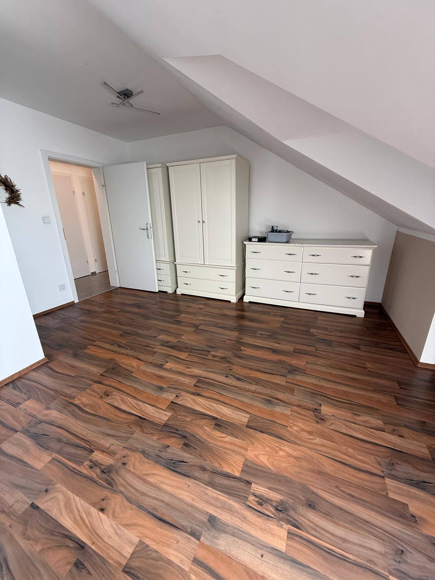 Geräumiges Schlafzimmer mit Laminatboden, Dachschrägen und weißem Kleiderschrank.