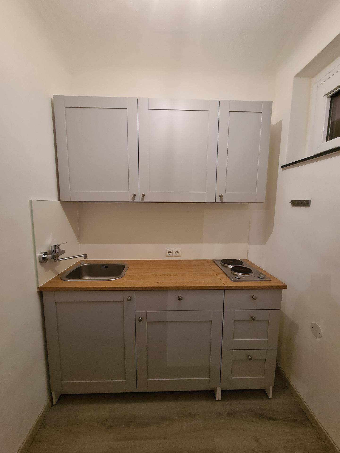 Kleine Küchenzeile mit grauen Schränken, Spüle, Kochfeld und Holz-Arbeitsplatte.
