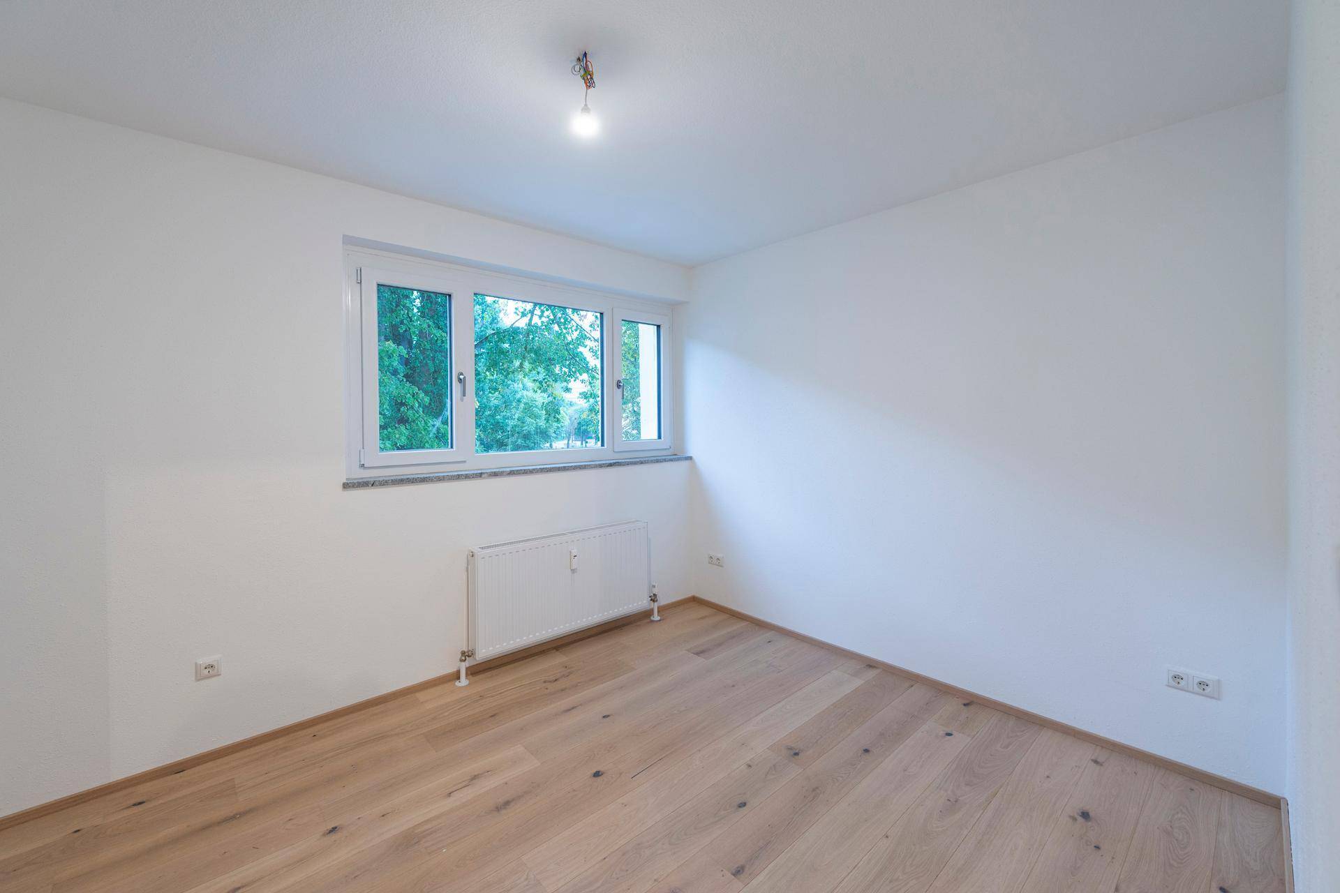 Helles Schlafzimmer mit Parkettboden und Blick ins Grüne.