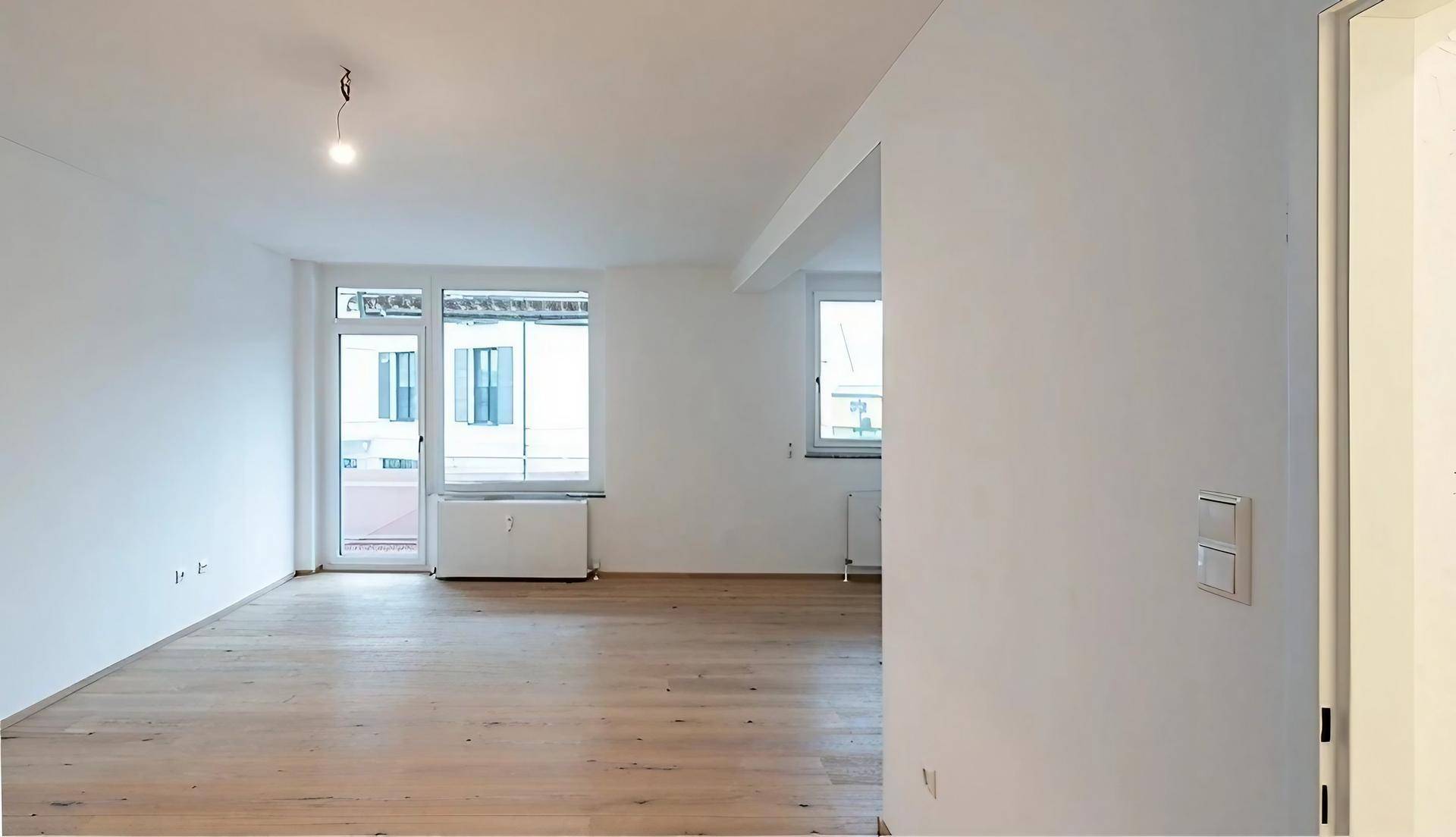 Helles Wohnzimmer mit Parkettboden und Zugang zu einem Balkon.