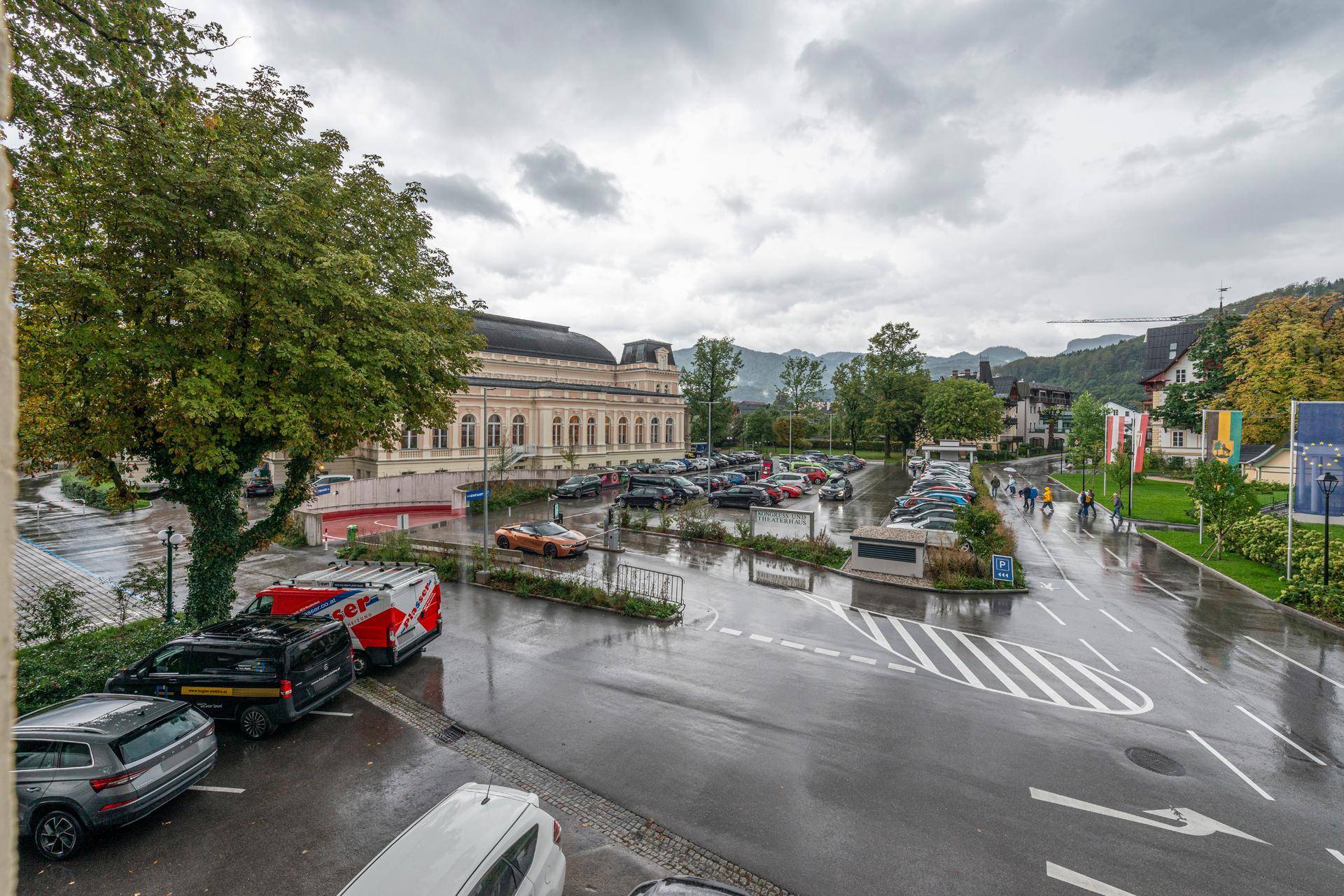 Außenansicht mit Parkplatz und historischem Gebäude unter bewölktem Himmel.