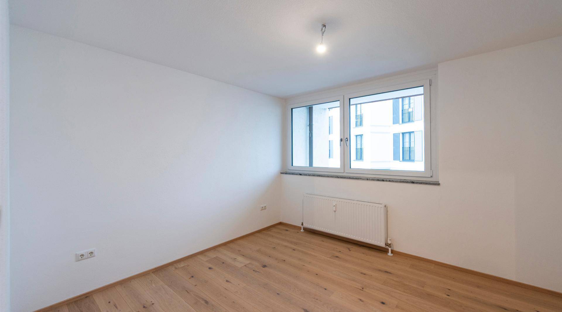 Schlafzimmer mit hellem Parkettboden und großem Fenster.