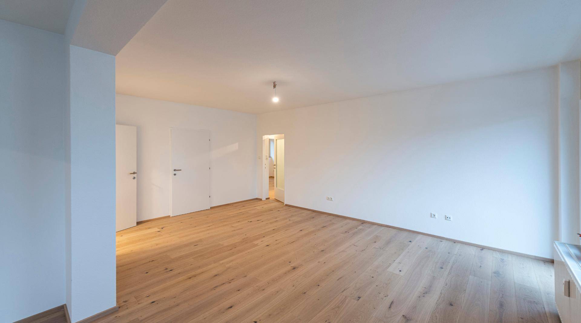 Weitläufiges Wohnzimmer mit hellem Parkettboden und mehreren Türen.