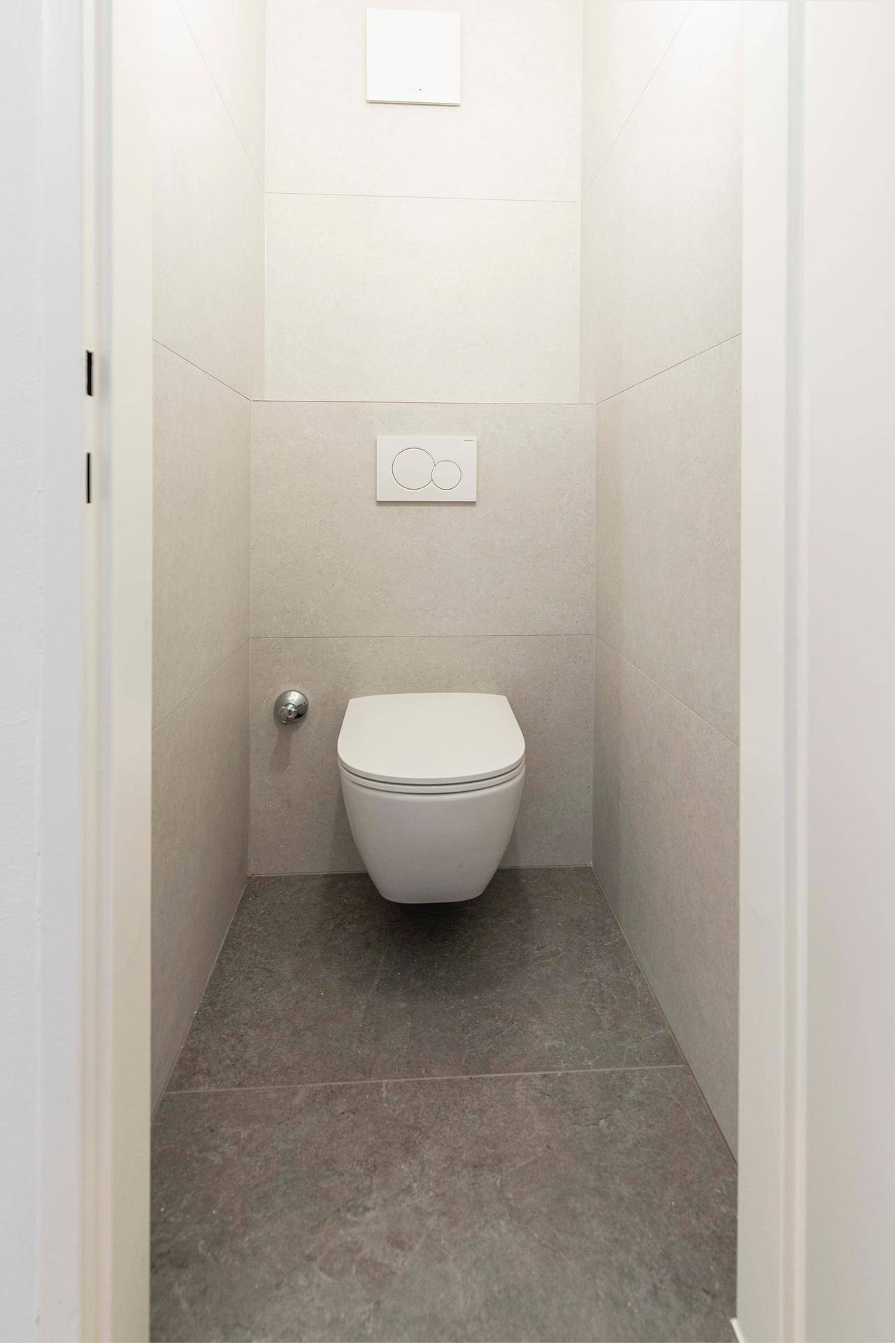 Separates WC mit wandhängender Toilette und modernen Fliesen.